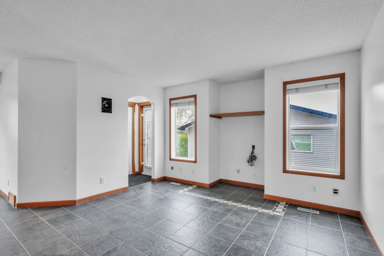 Empty room with dark slate tile flooring, white walls, wood trim windows, and built-in shelving nook.