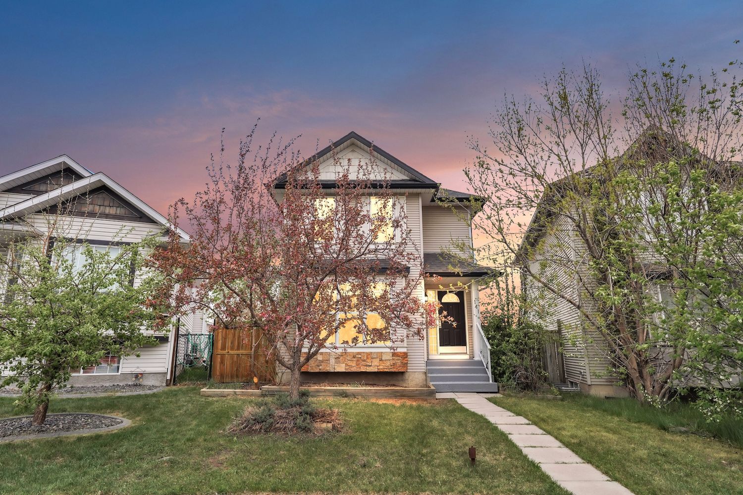 Two-story home with blooming pink tree and lush green lawn photographed at golden hour sunset.