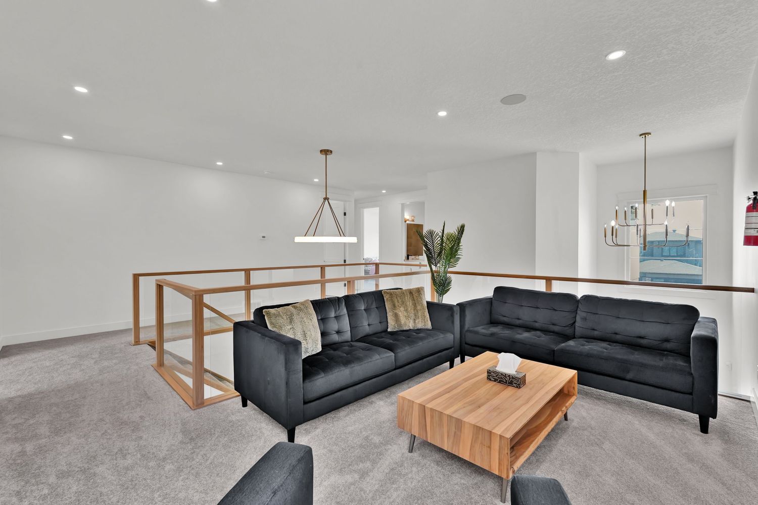 Spacious upper-level living area with black sectional sofa, wood coffee table, and open railing staircase.