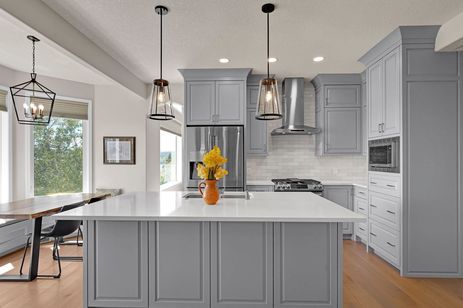Modern kitchen with gray cabinets, white quartz island, stainless steel appliances, pendant lights, and hardwood floors.