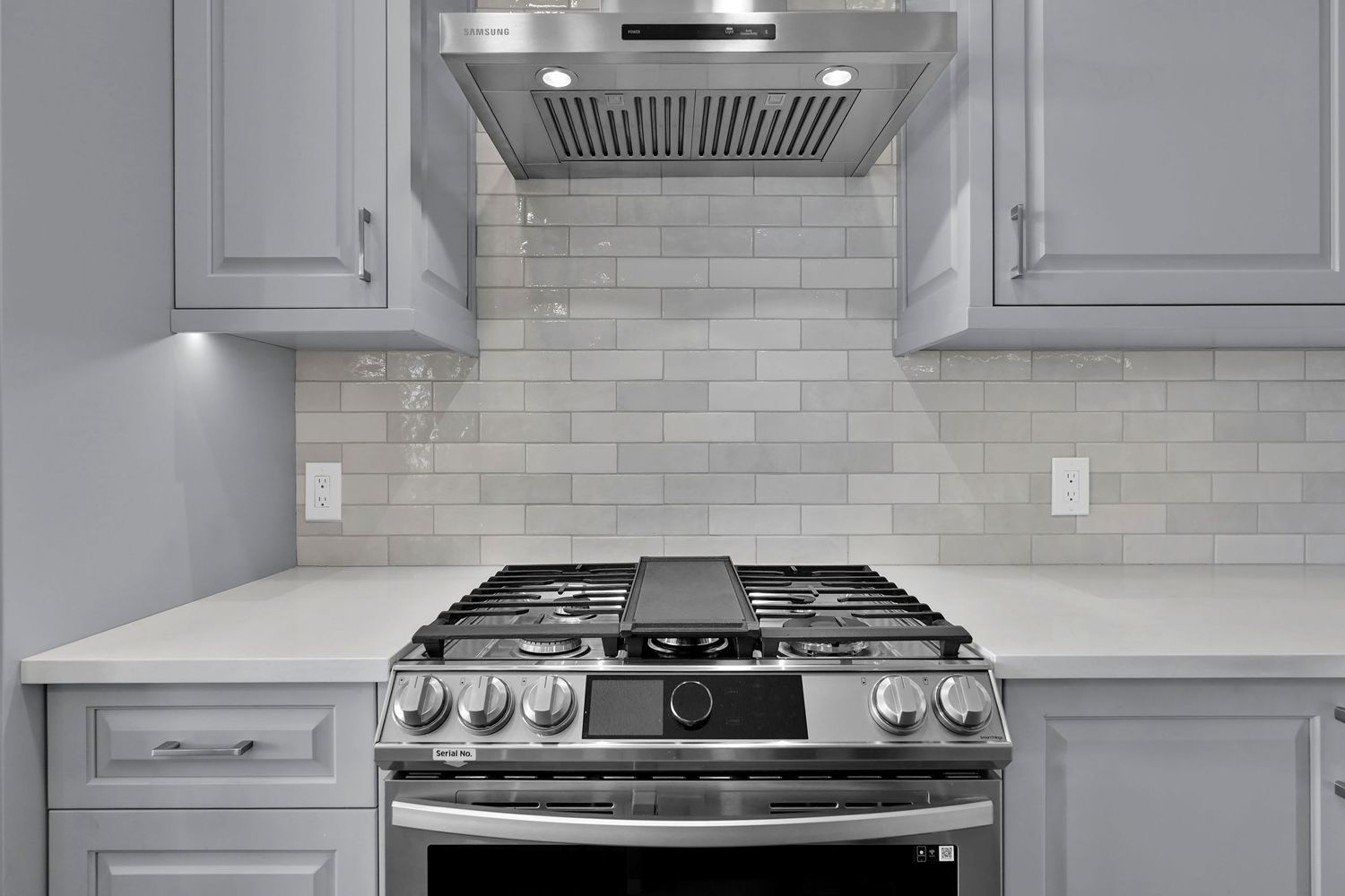 Modern kitchen with stainless steel gas range, white subway tile backsplash, and gray shaker cabinets with range hood.