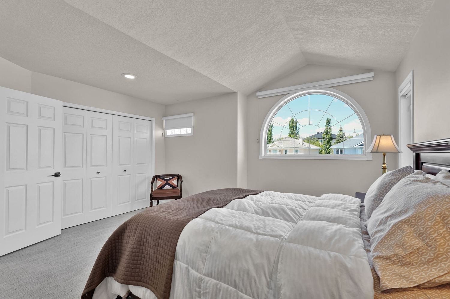 Bright bedroom with vaulted ceiling, arched window, large closet, and neutral decor with hardwood floors.
