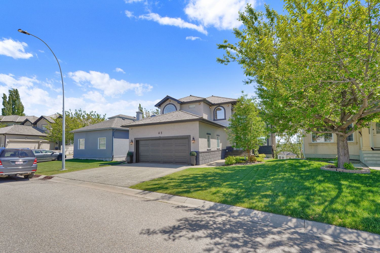 Two-story suburban home with double garage, manicured lawn, and mature trees on a quiet residential street.