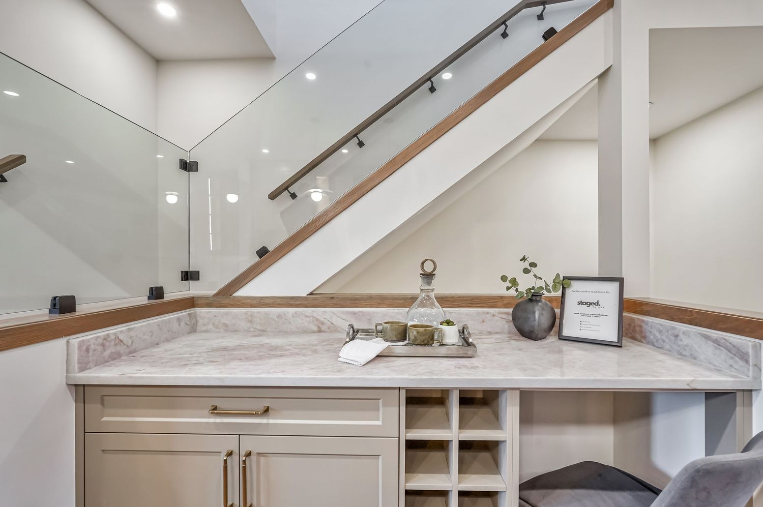 Under-stair built-in desk with marble countertop, wine rack, and glass railing staircase in modern home.