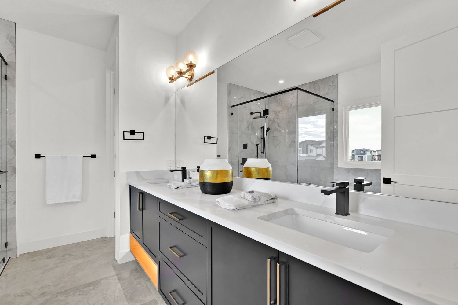 Elegant double vanity bathroom with gray cabinets, white quartz countertop, black fixtures, and glass shower.