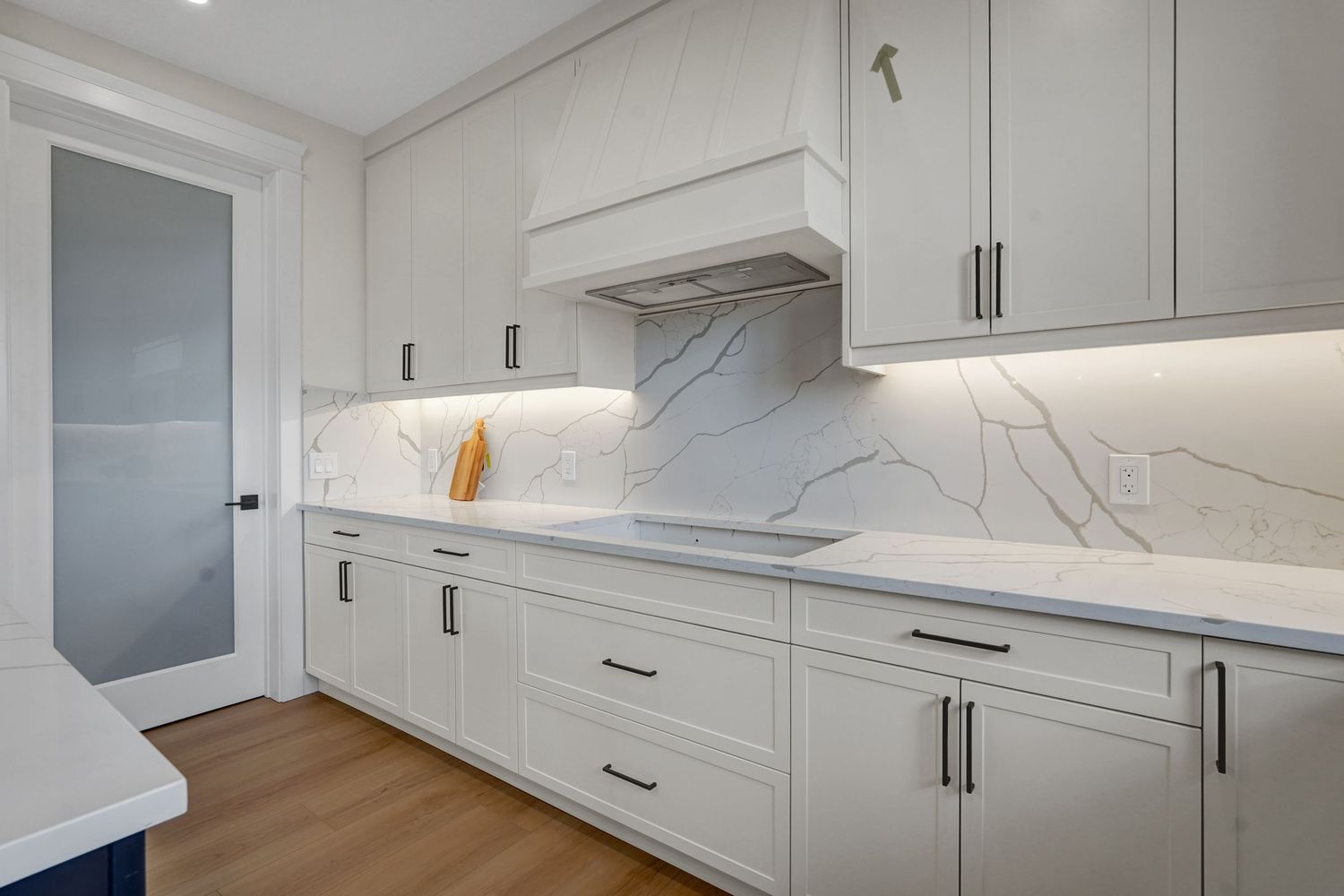 Modern white kitchen with marble backsplash, shaker cabinets, quartz countertops, and stainless range hood.