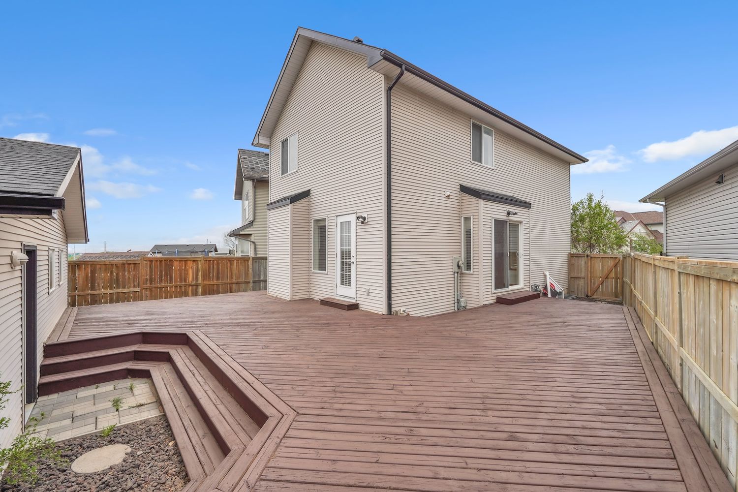 Expansive wood deck with fenced backyard, steps to yard, and two-story home exterior view.