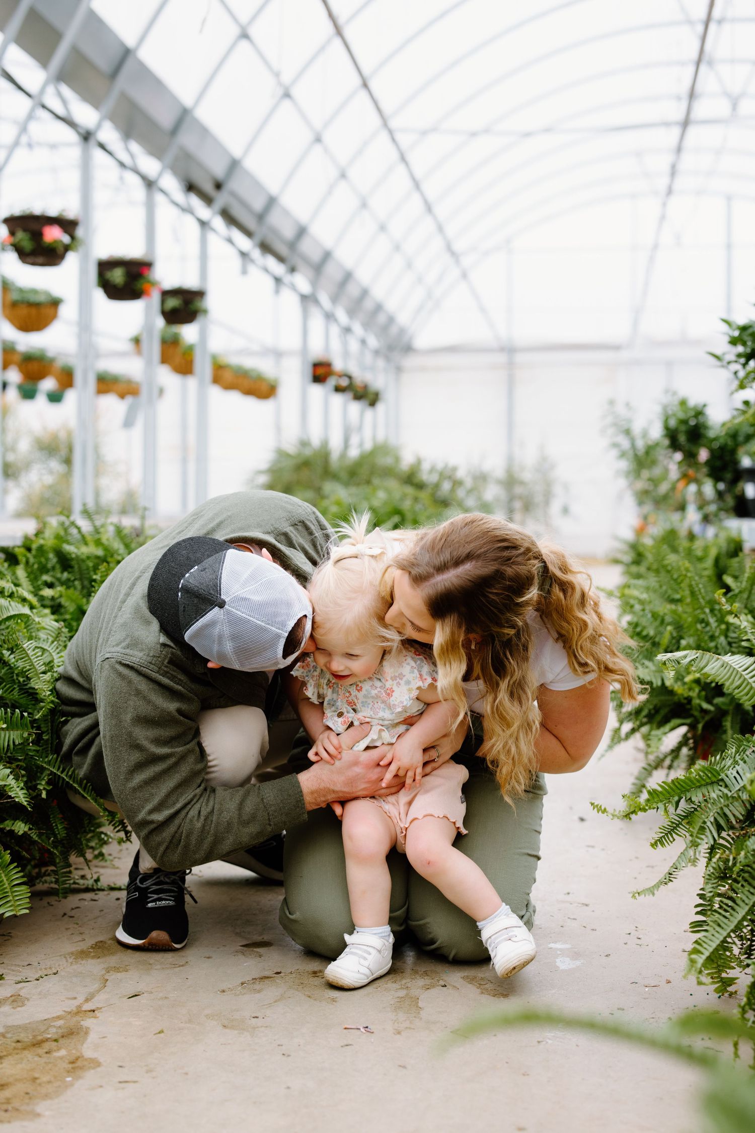 A touching moment shared in a sunlit greenhouse filled with lush green ferns and hanging baskets.