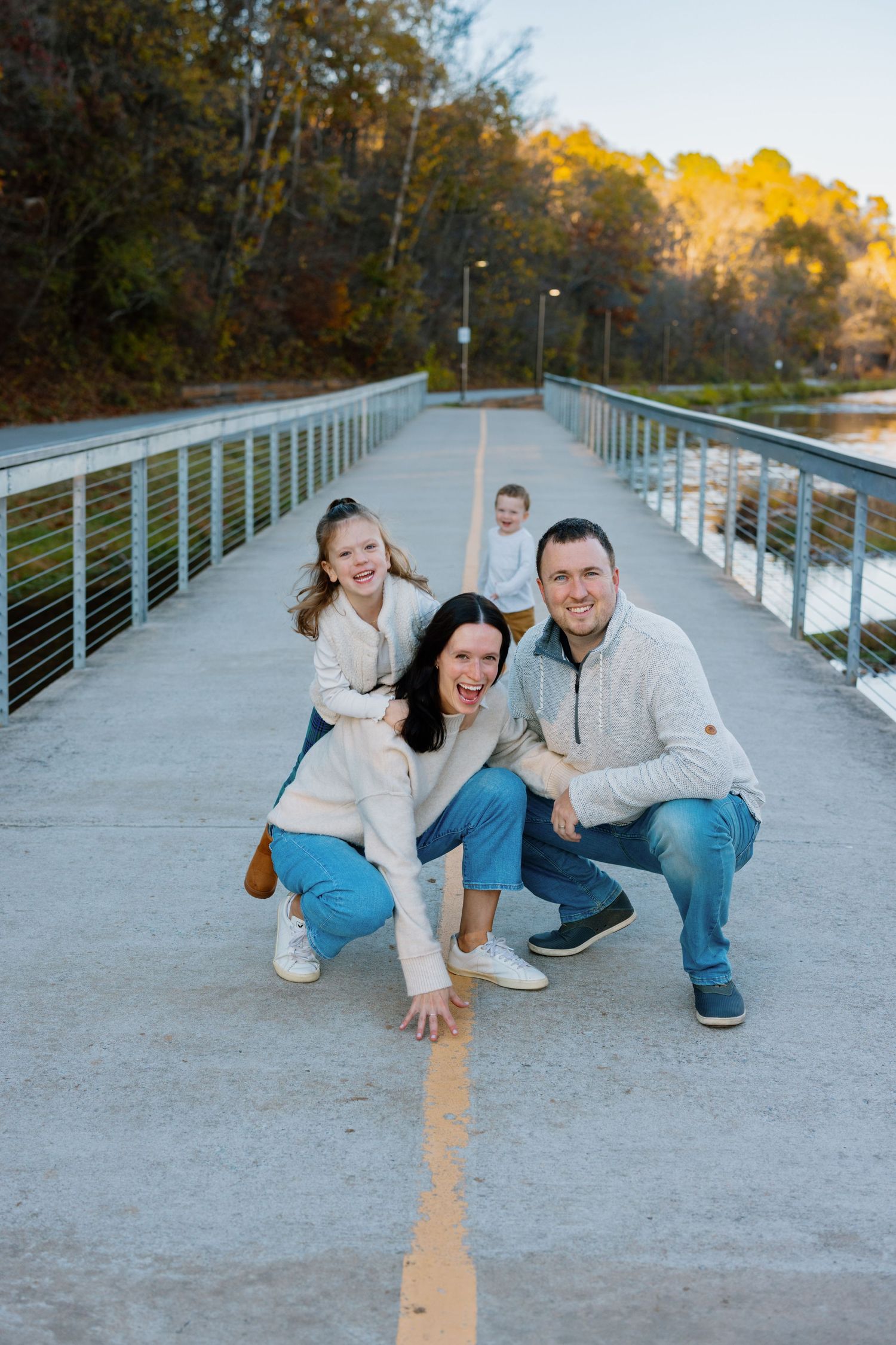 A group poses together on a modern pedestrian bridge with metal railings during golden hour in autumn weather.