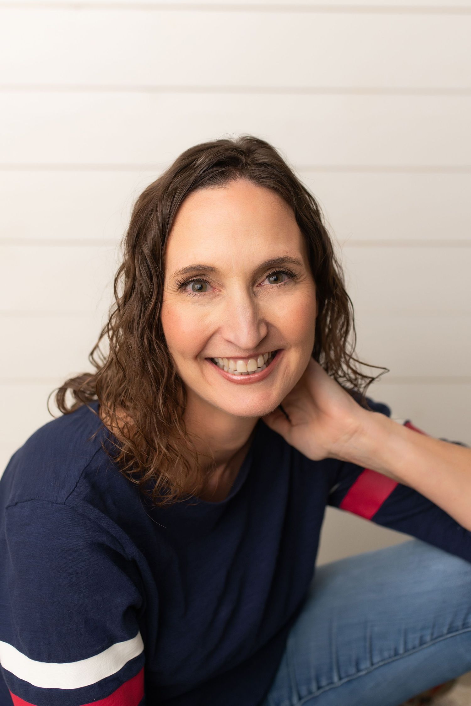 Person in navy striped sweater poses against white wall background.
