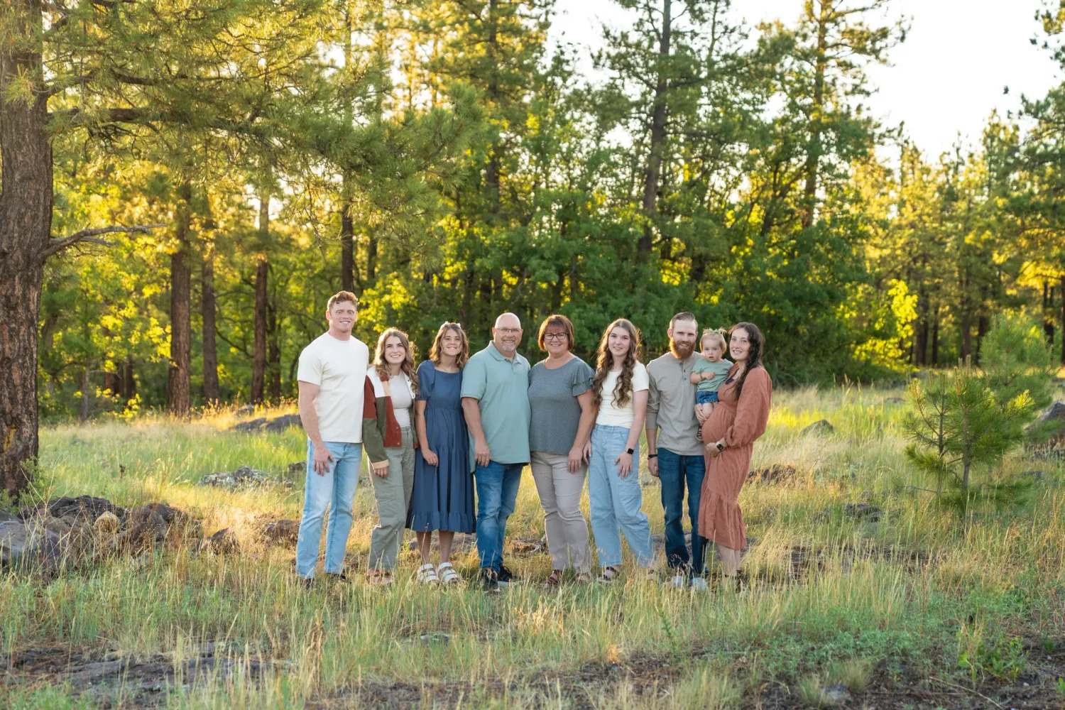 Family group portrait in a sunlit pine forest clearing during golden hour in Flagstaff, Arizona.