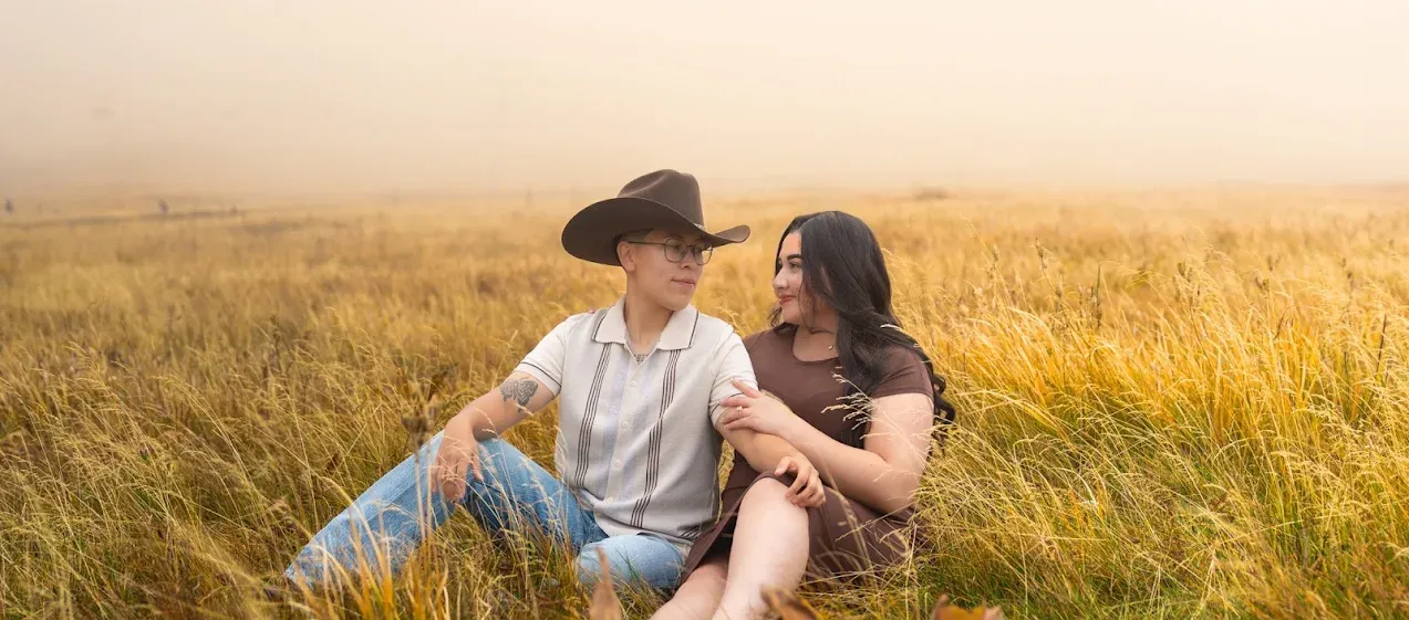 Western-style couple sitting together in a foggy mountain field at Snowbowl in Flagstaff, Arizona during a romantic session.