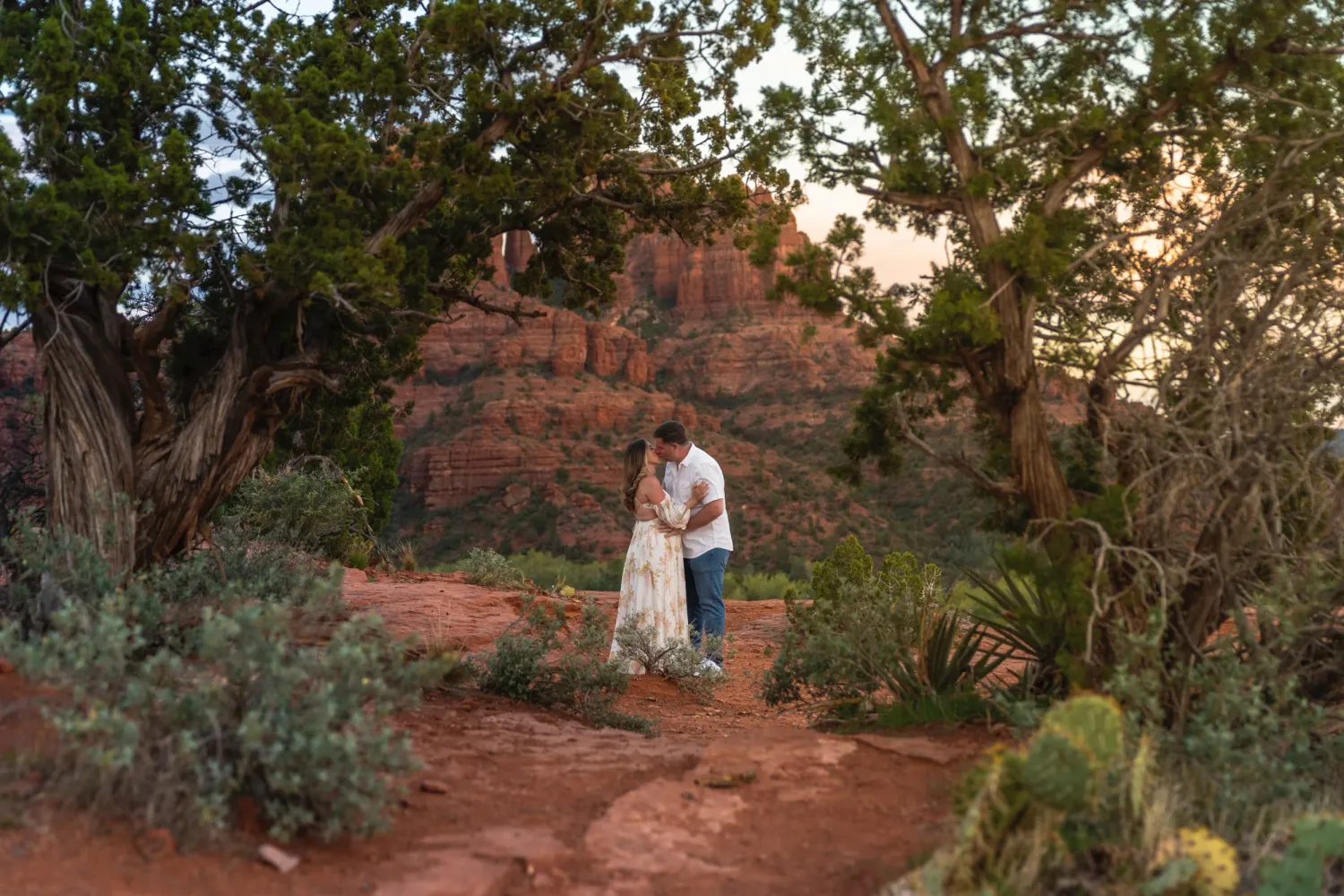 Maternity portraits of an expecting couple framed by trees at Secret Slick Rock in Sedona, Arizona.