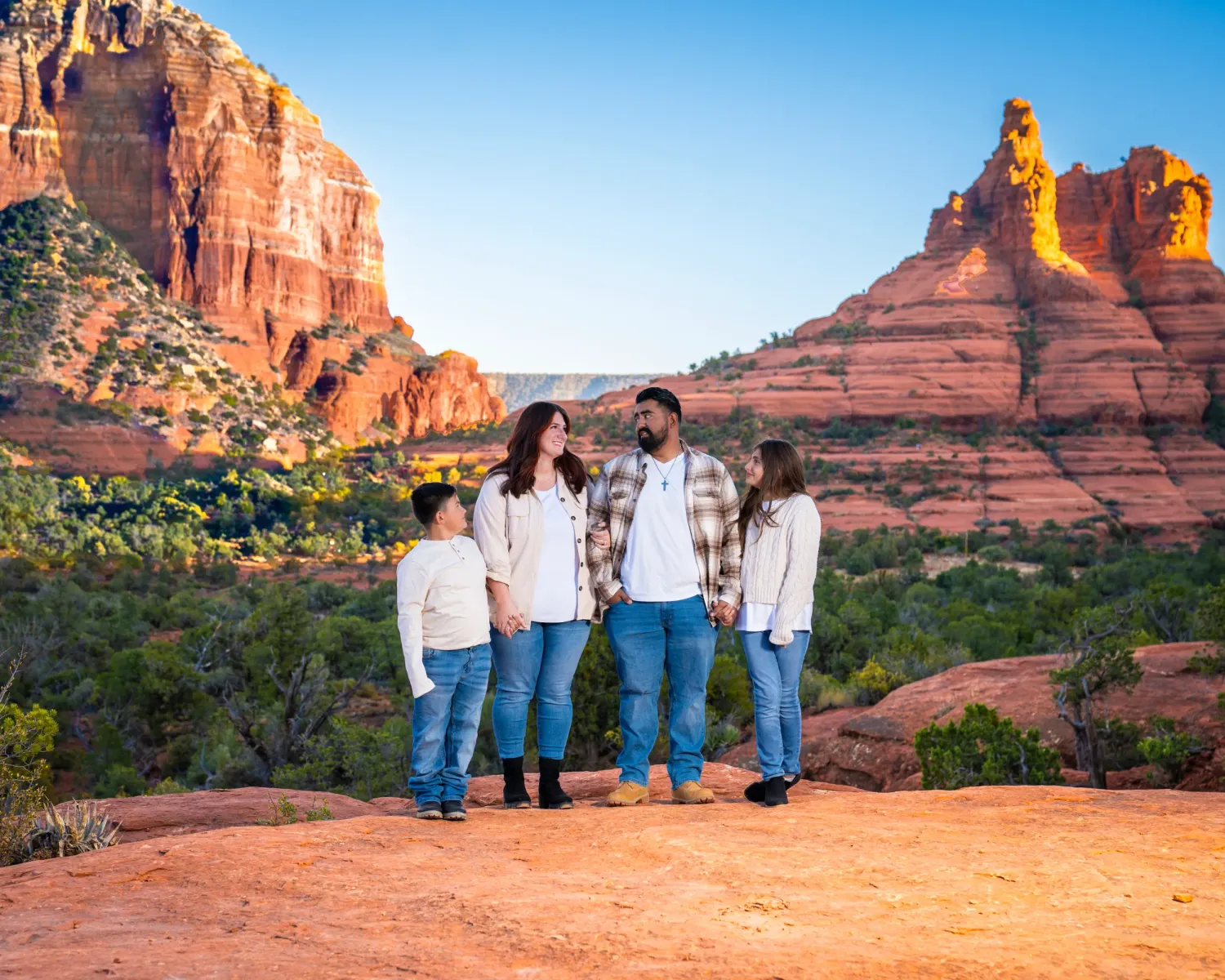 Family of four walking together on red rock terrain with Sedona buttes in the background at Yavapai Vista in Sedona, Arizona.