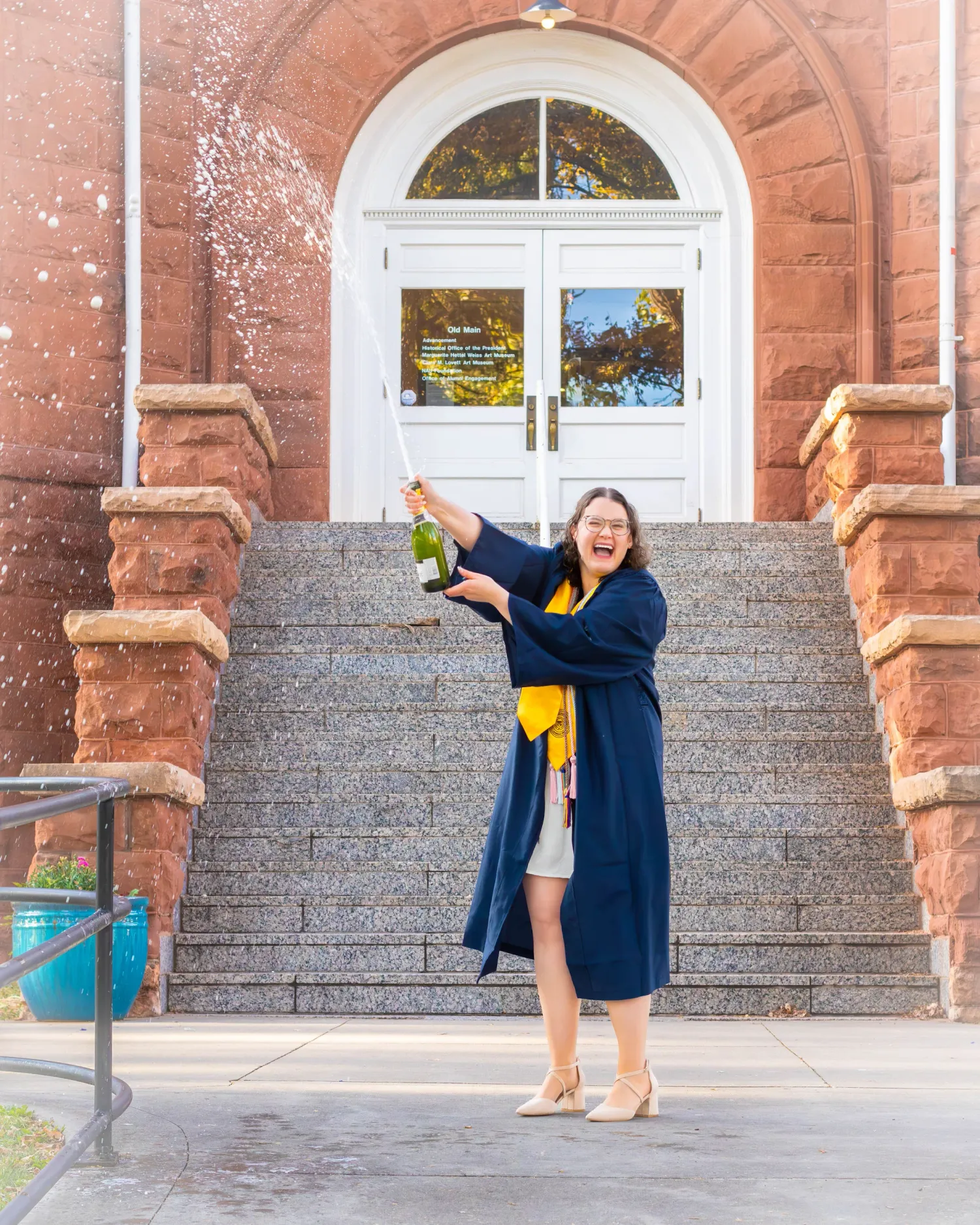 Senior girl celebrating graduation with a champagne pop at Old Main, Northern Arizona University in Flagstaff, Arizona.