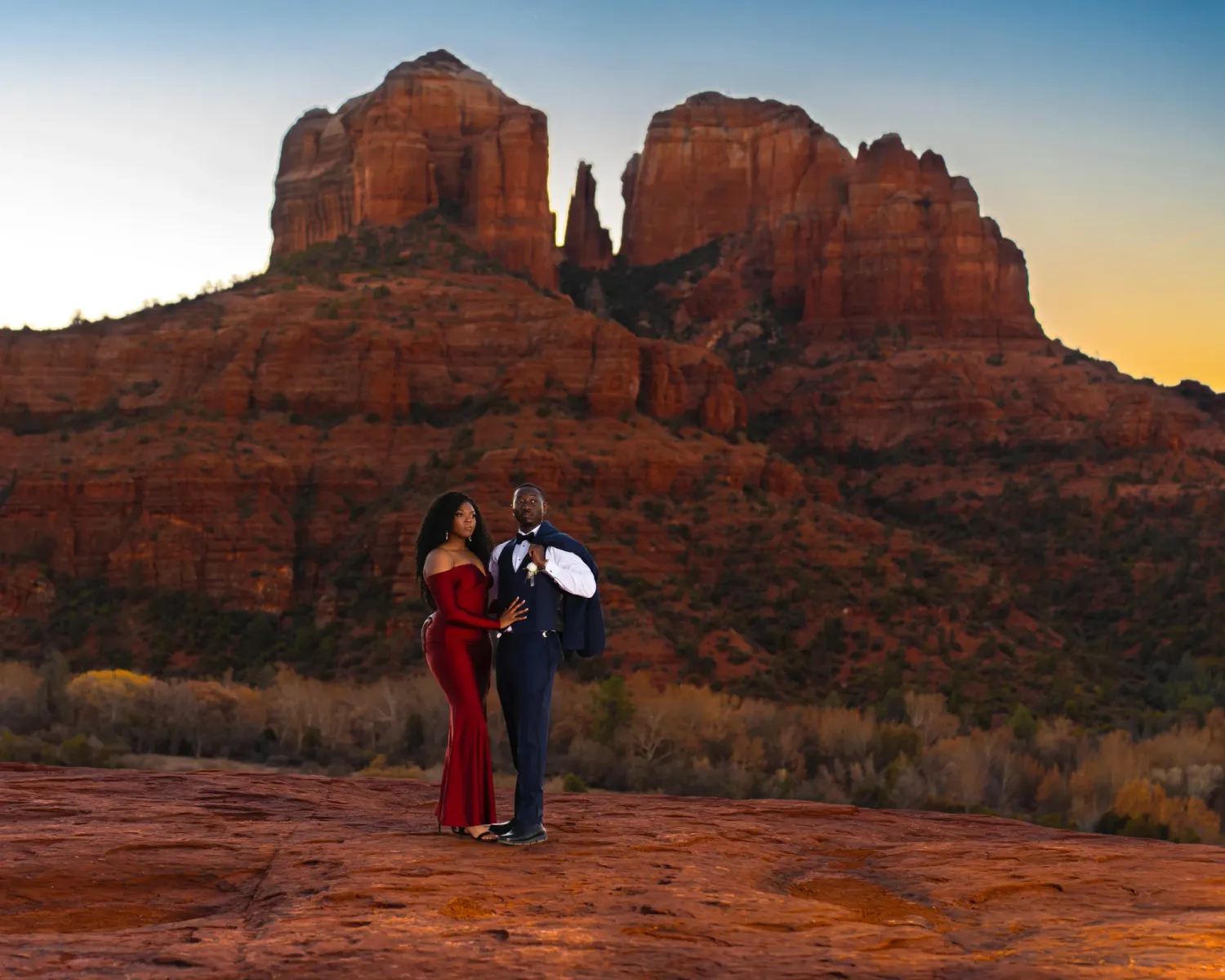 Couple in formal attire at sunrise with Cathedral Rock and dramatic red rock formations in Sedona, Arizona.