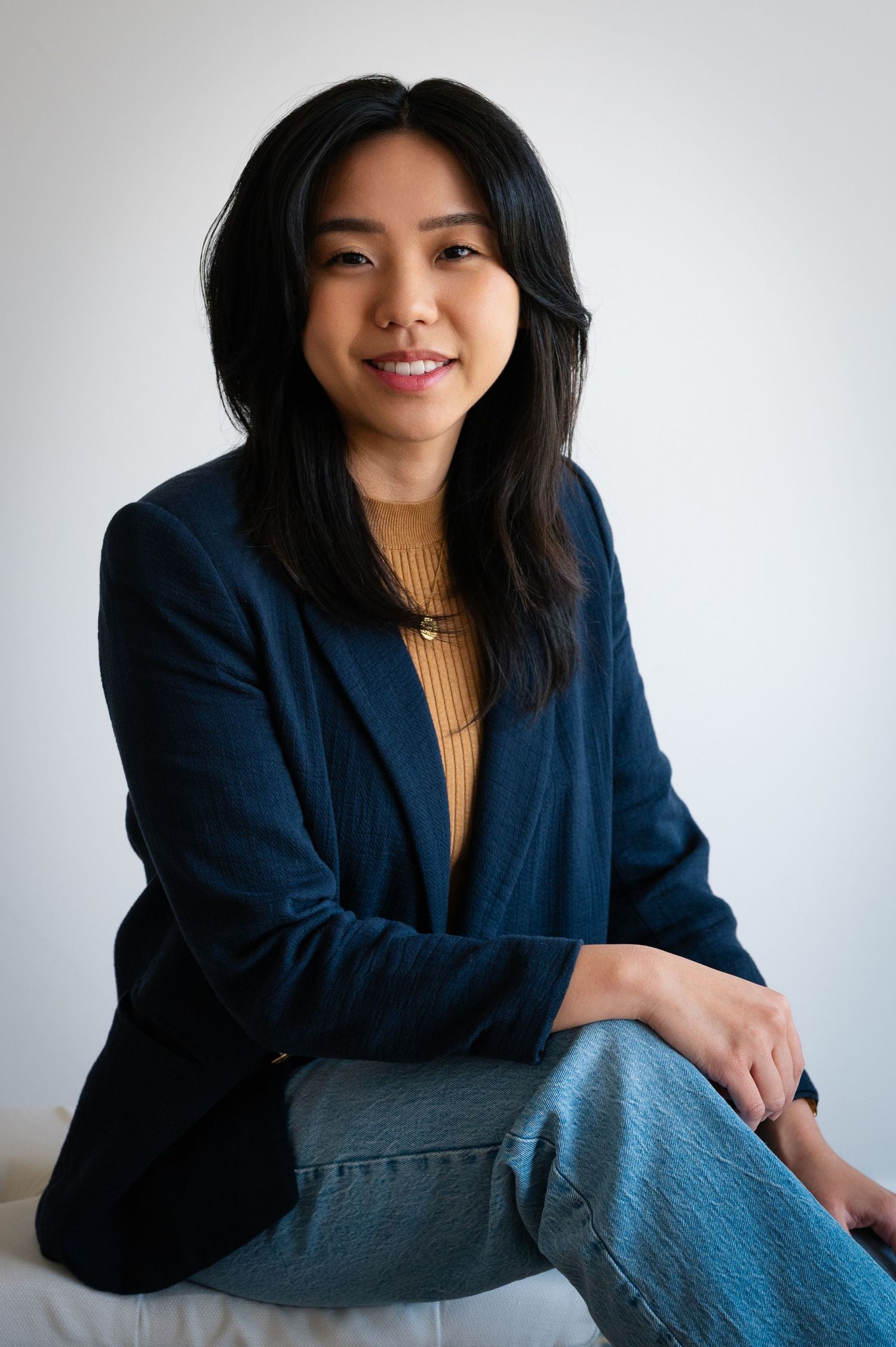 Professional portrait featuring a navy blazer and tan sweater against a white background.