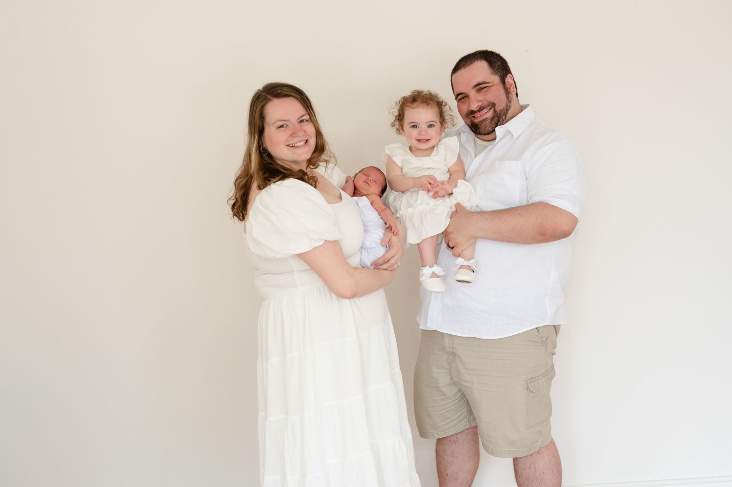 A family with a toddler and newborn in a studio portrait.