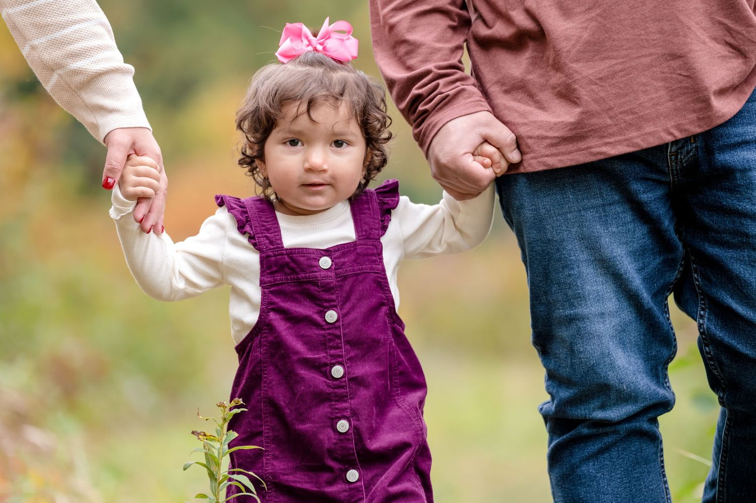 A young girl walks through the woods holding her parents hands.