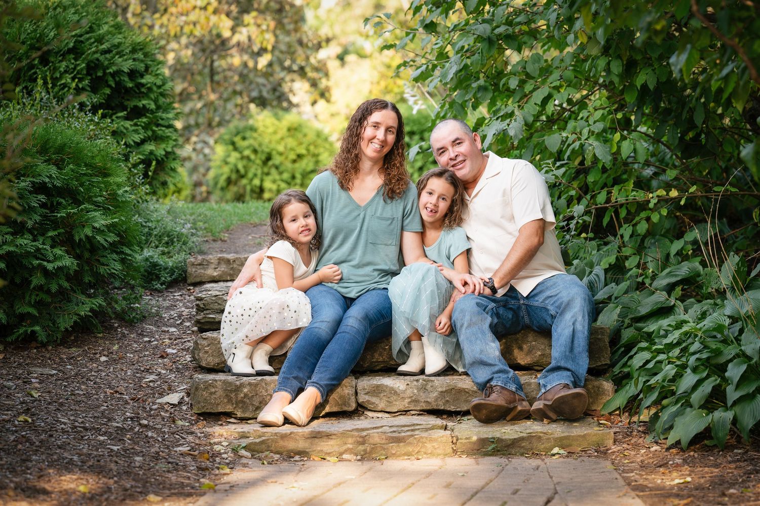 A family of four sits together on rocks along a wooded trail.