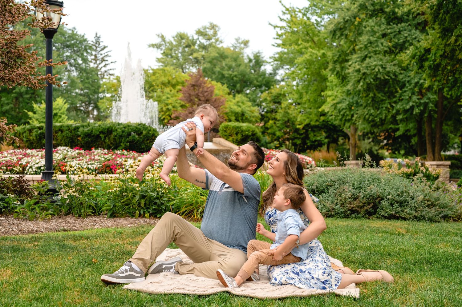 A family enjoys a picnic on a blanket in a park surrounded by blooming flowers and greenery.