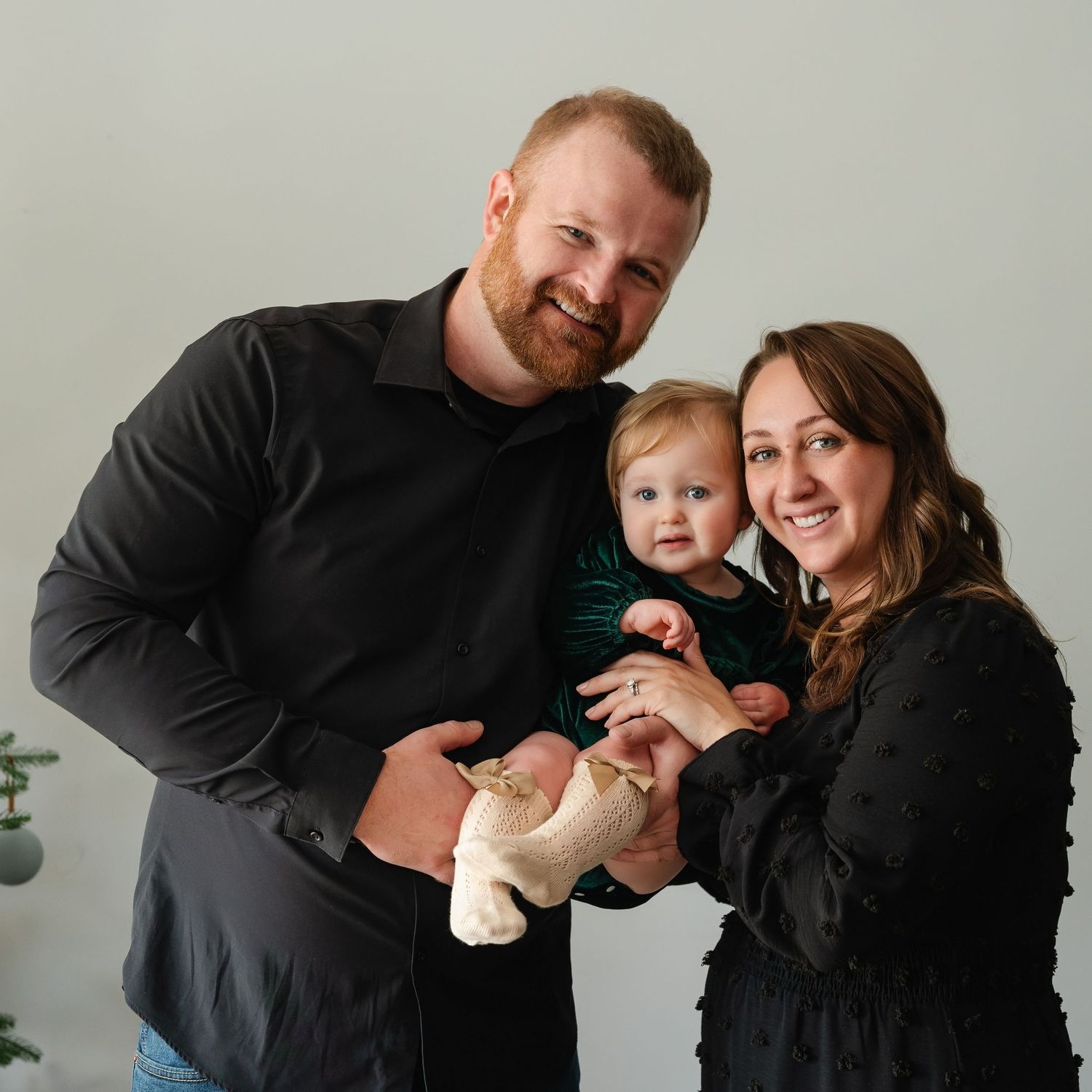 A family wearing coordinating black outfits poses together in a bright indoor setting.