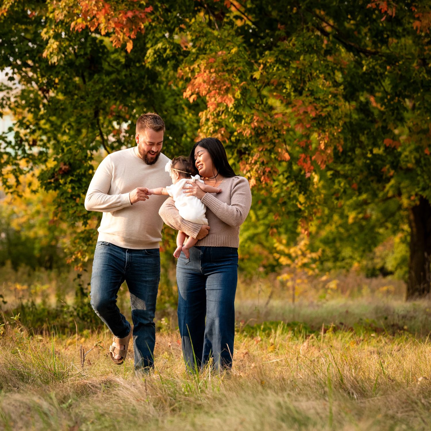 Family walking together through golden autumn field during sunset photoshoot.