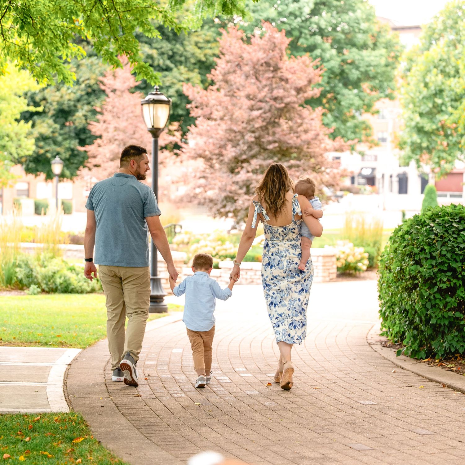 A family walks hand in hand down a brick path surrounded by landscaped gardens and trees.