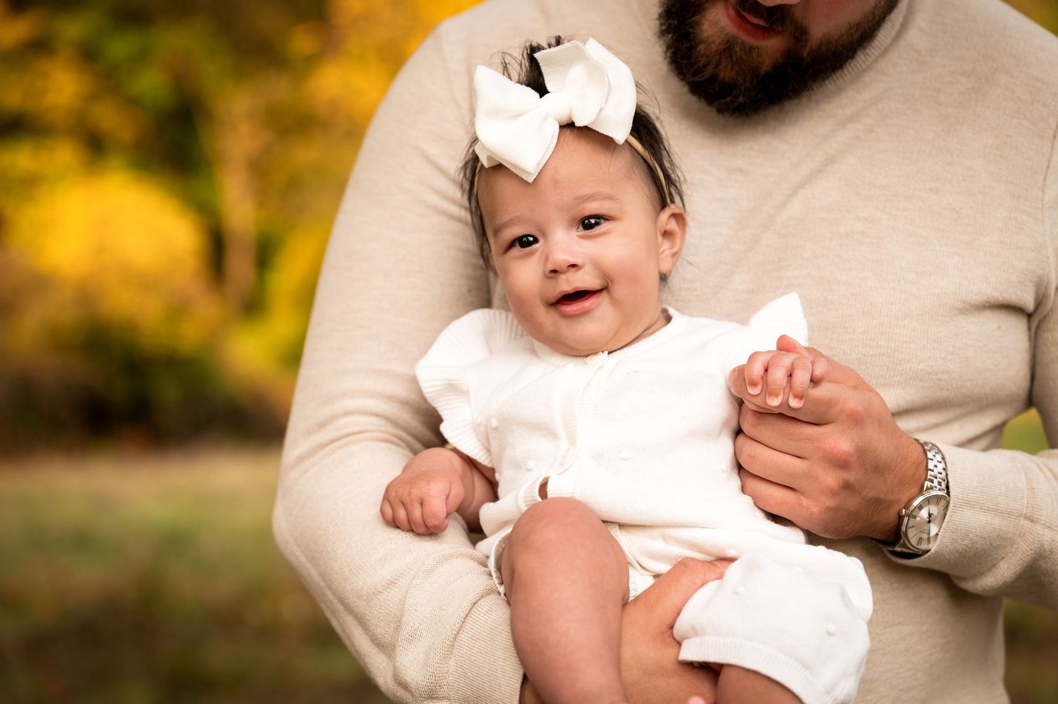 Playful outdoor baby photography session with cream sweater against autumn backdrop.