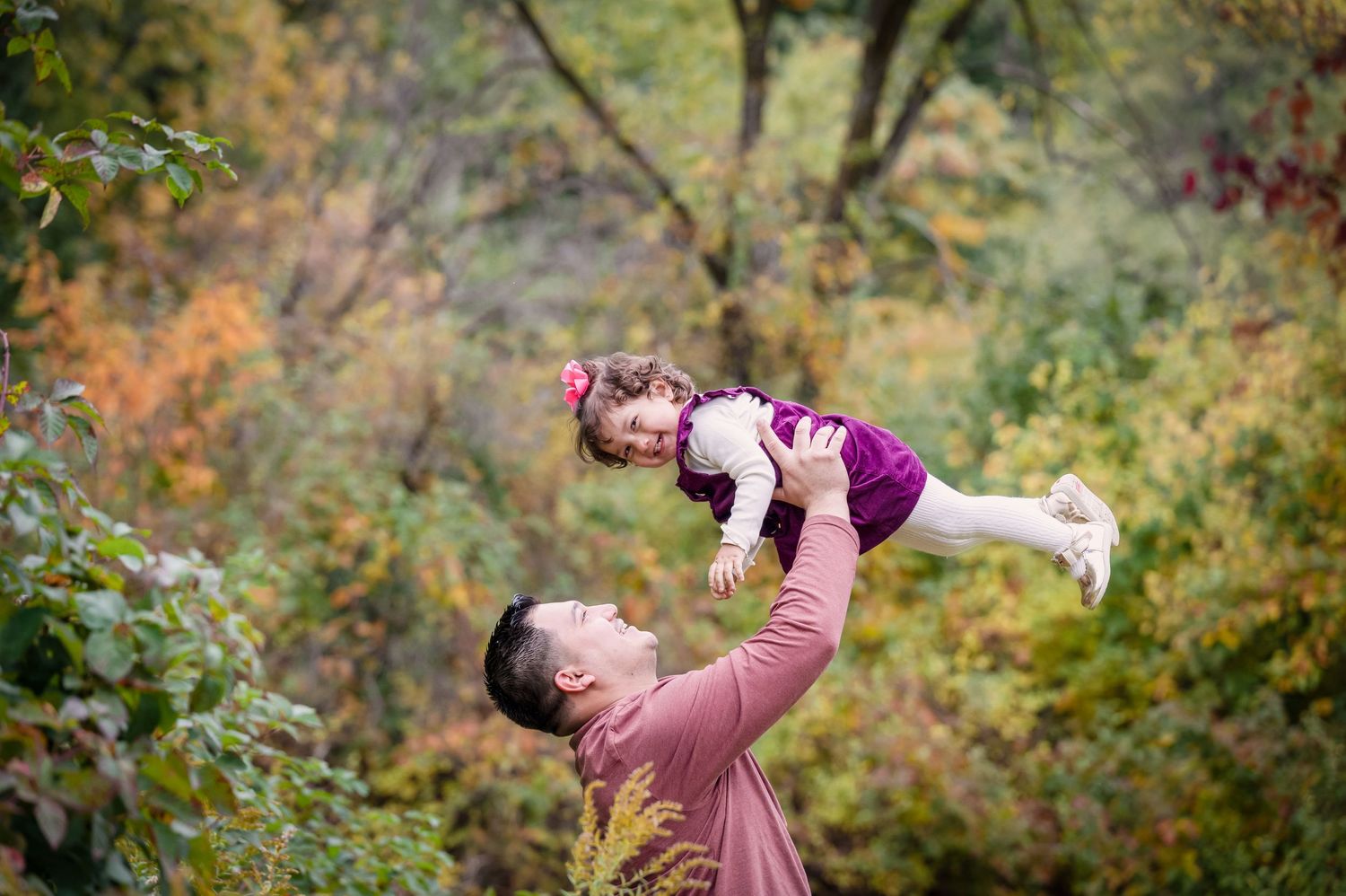 A father lifts his daughter up as she giggles and looks at the camera.