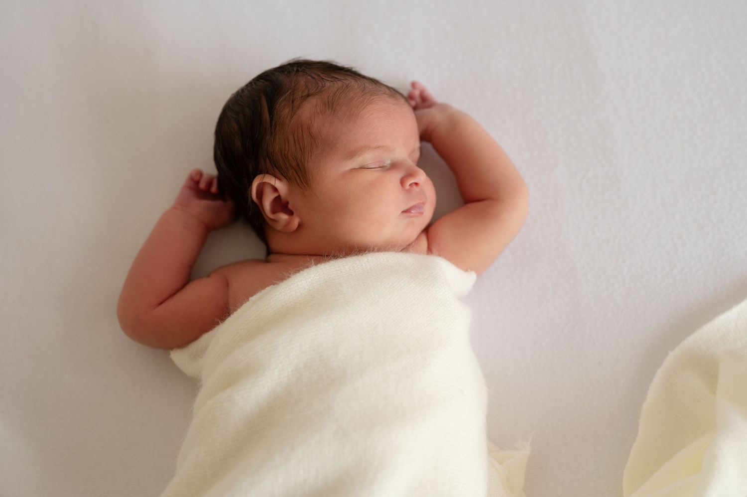 A newborn baby sleeps peacefully wrapped in soft cream-colored fabric.