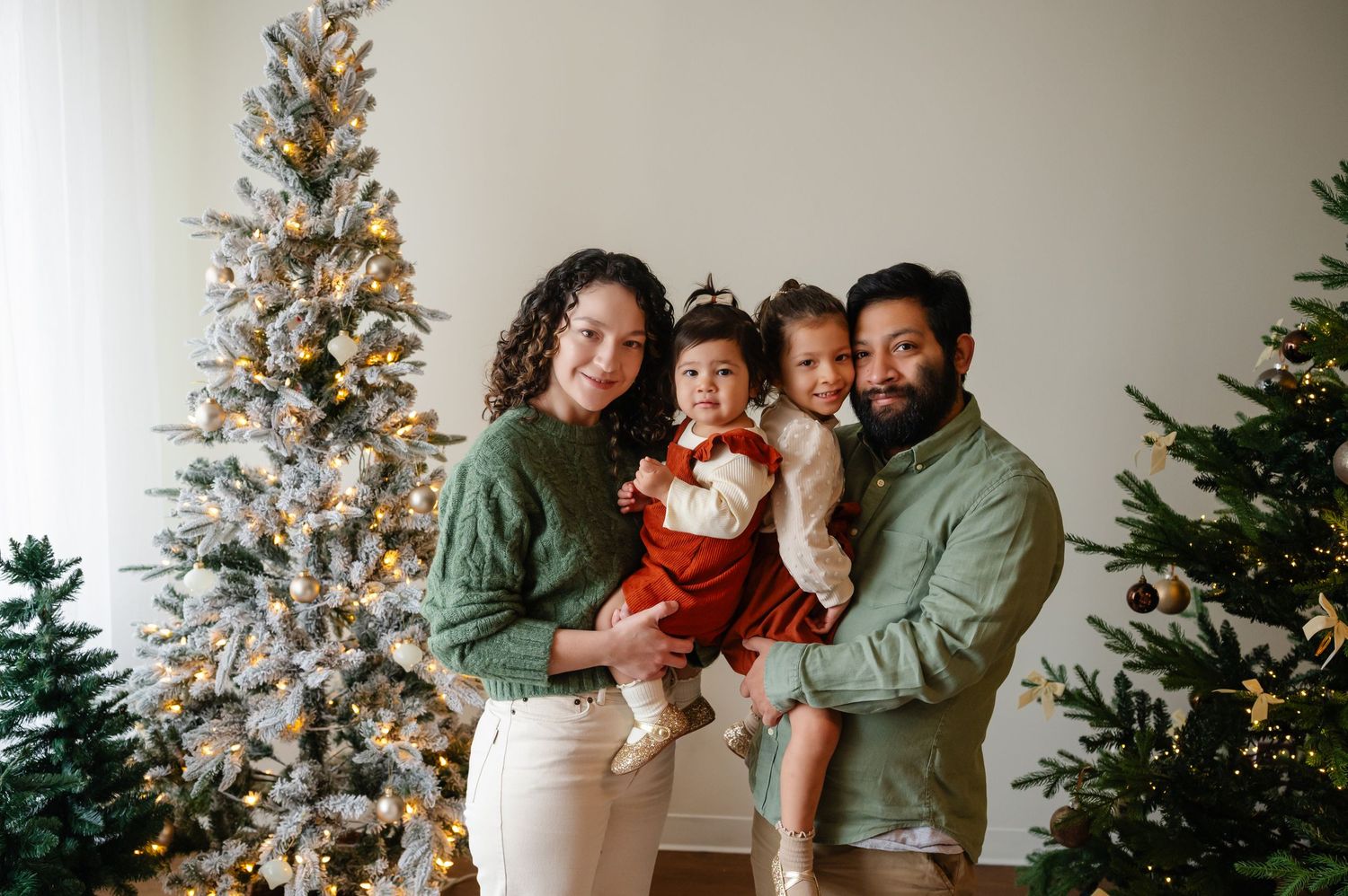 Family members cuddle close for holiday portrait by decorated Christmas tree.