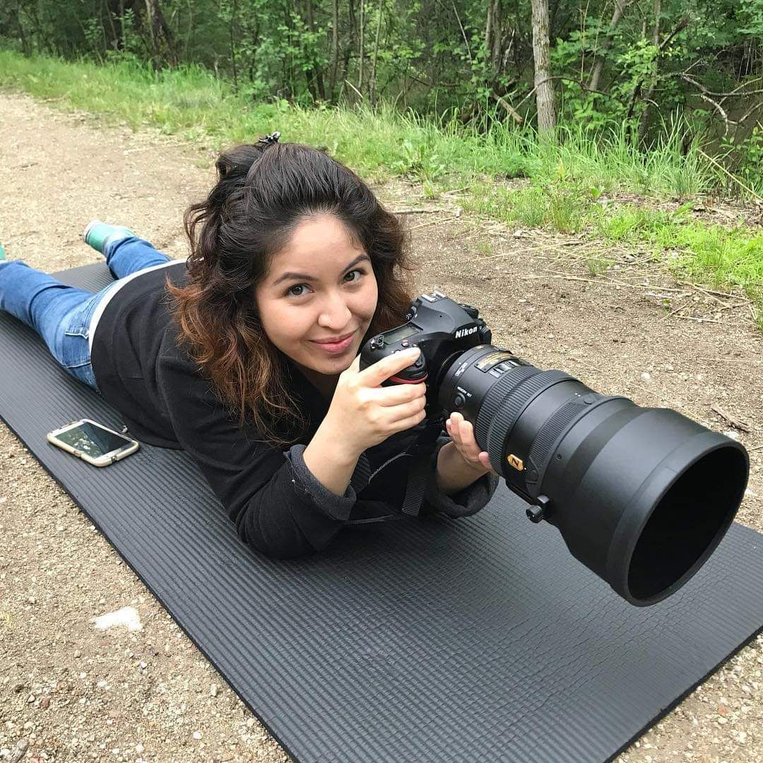 A photographer lies on a yoga mat with professional camera equipment outdoors.