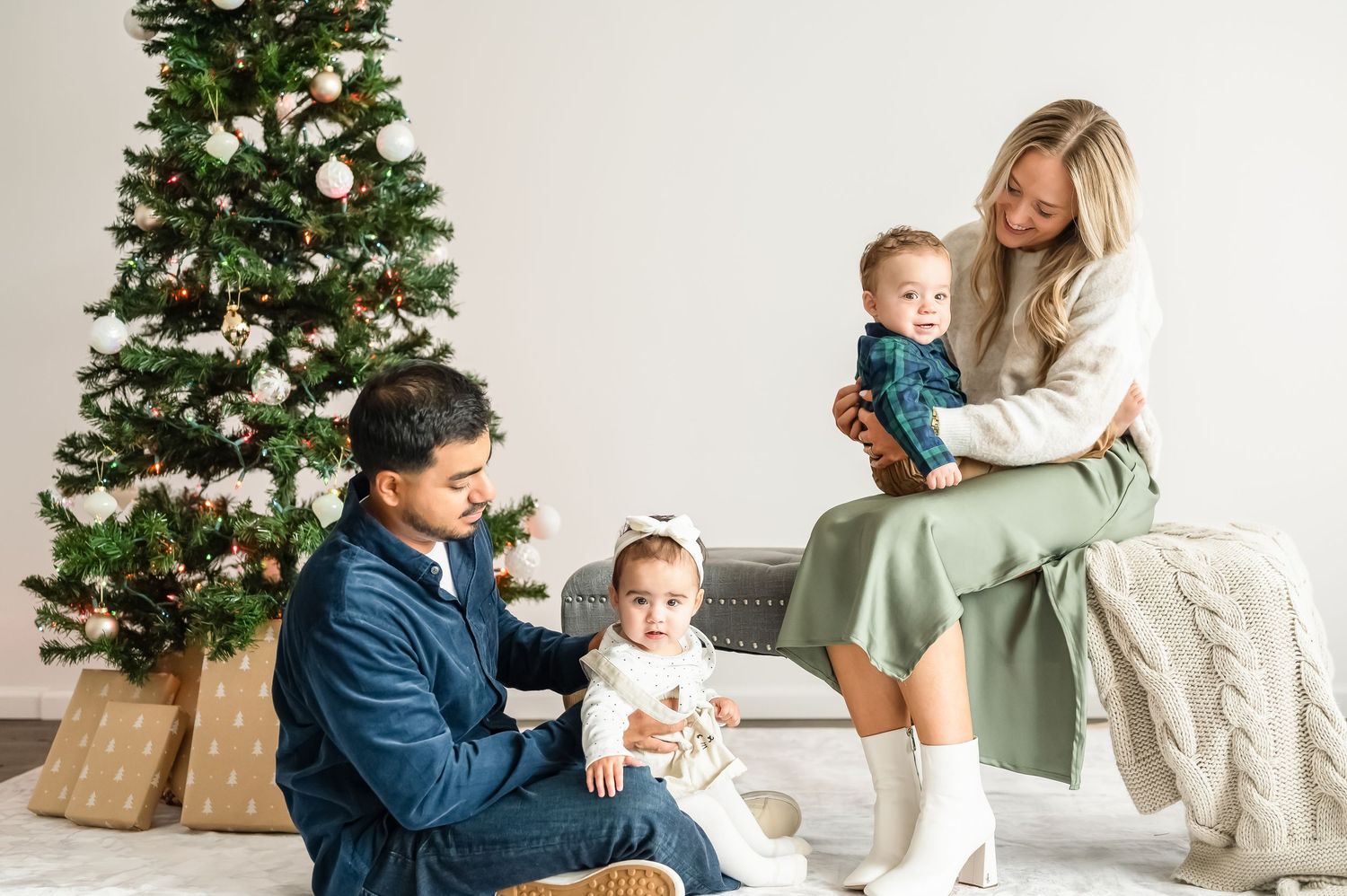 A family sits together by a decorated Christmas tree in a cozy living room setting.