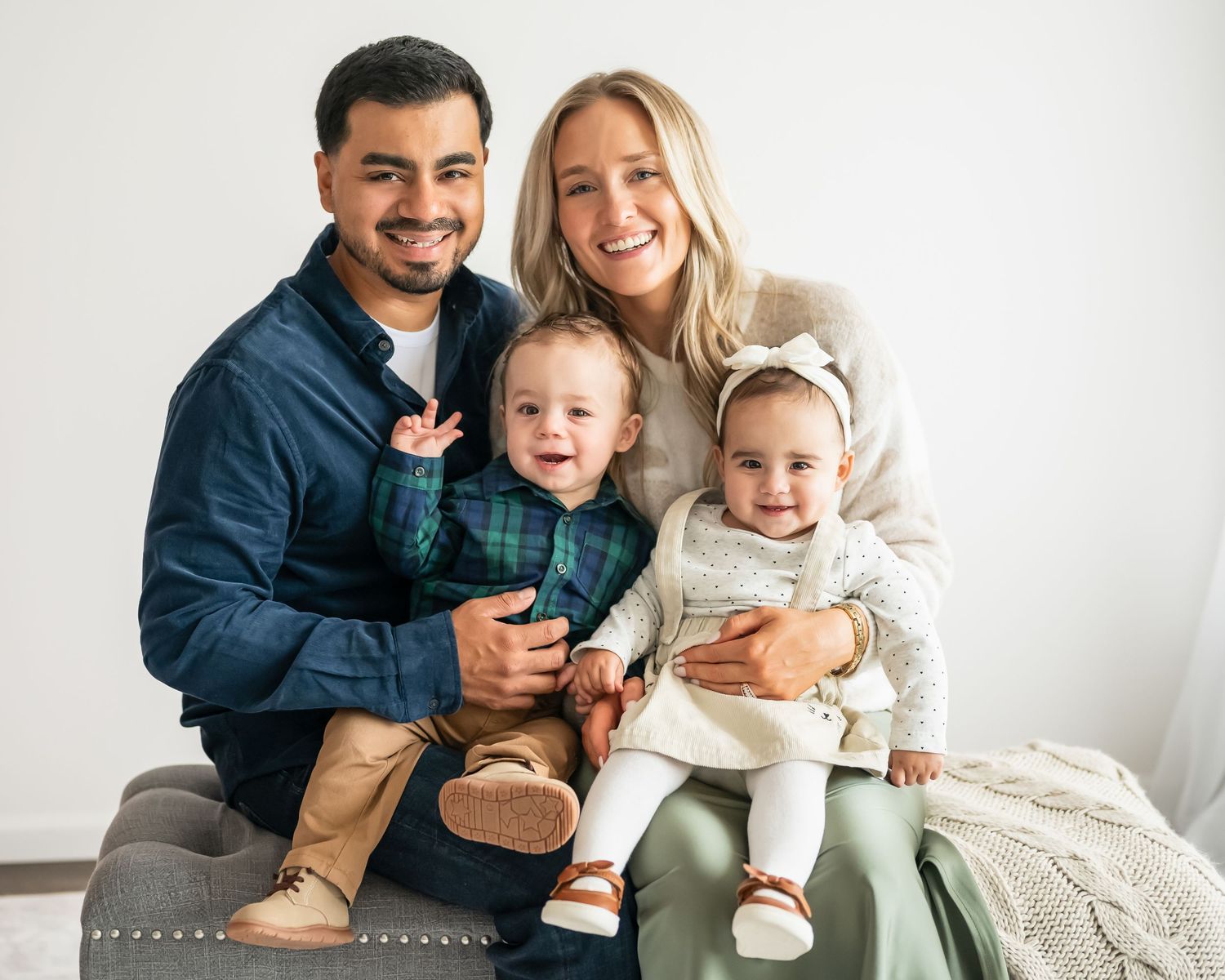 A happy family of four poses together against a white background.