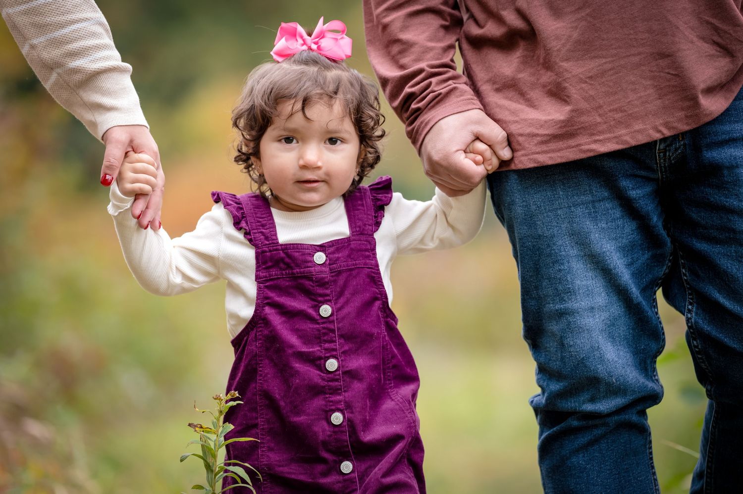 A young girl walks through the woods holding her parents hands.