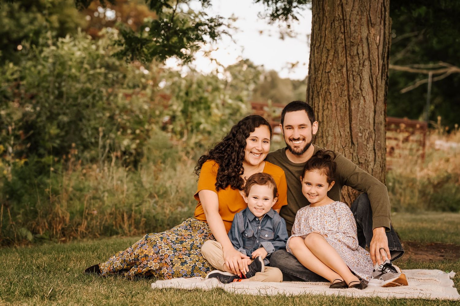A family sits together on a blanket in a sun-dappled autumn field.