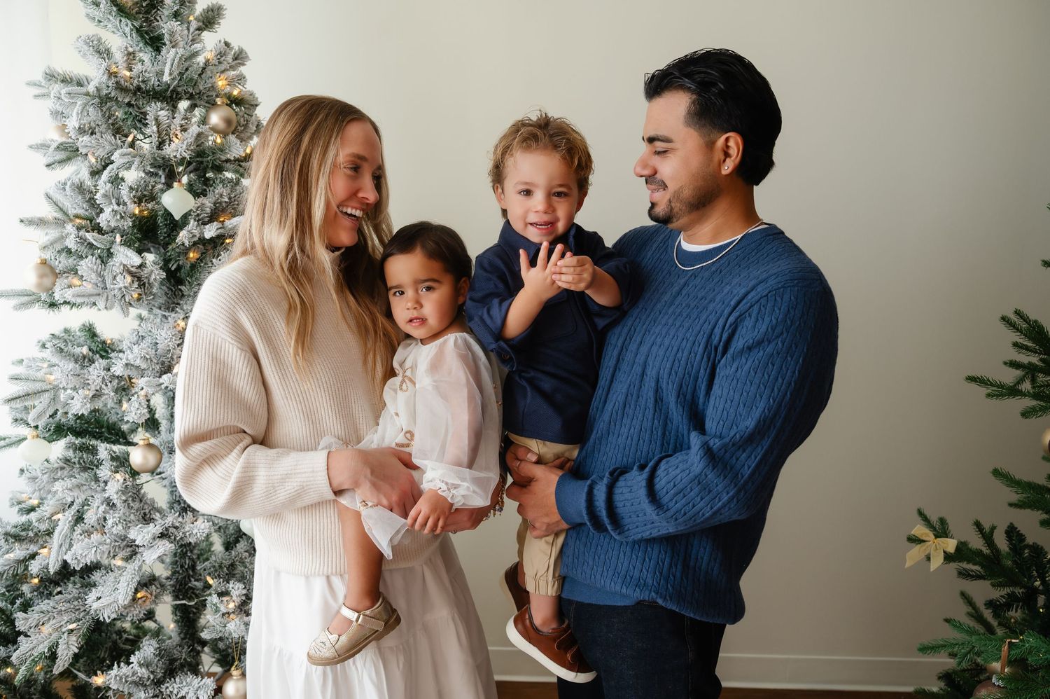 Family in coordinated winter outfits poses together by decorated Christmas tree.