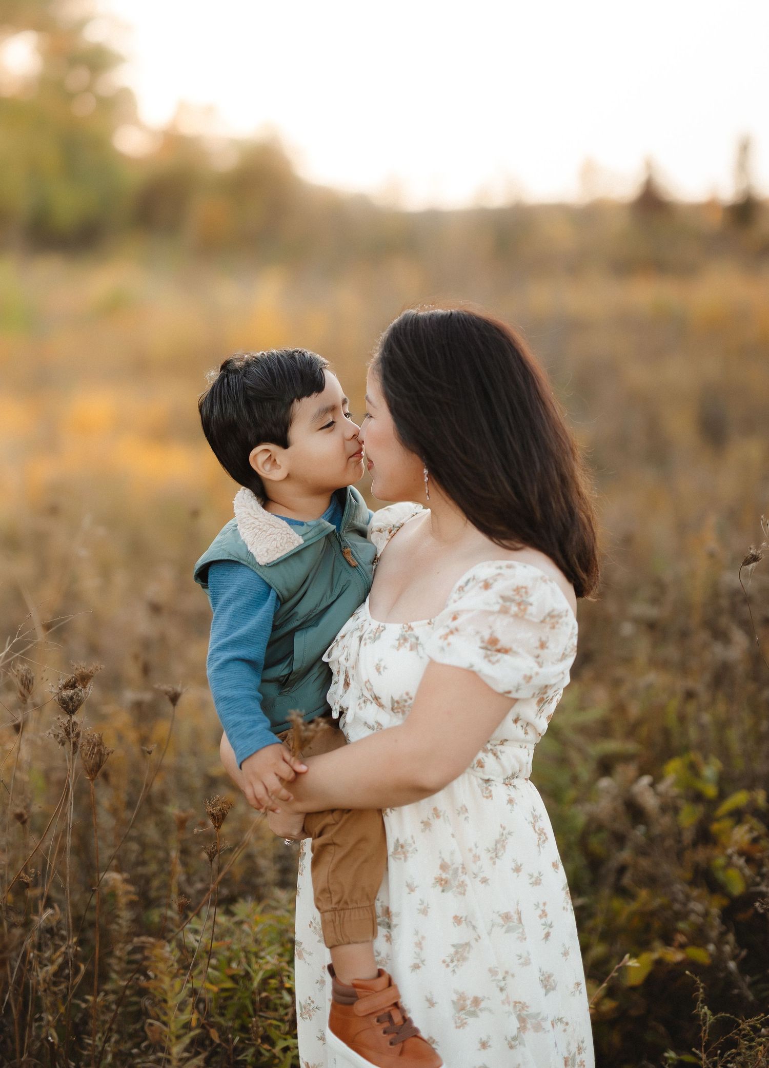 A tender moment between a mom and her son captured in a golden field during sunset.