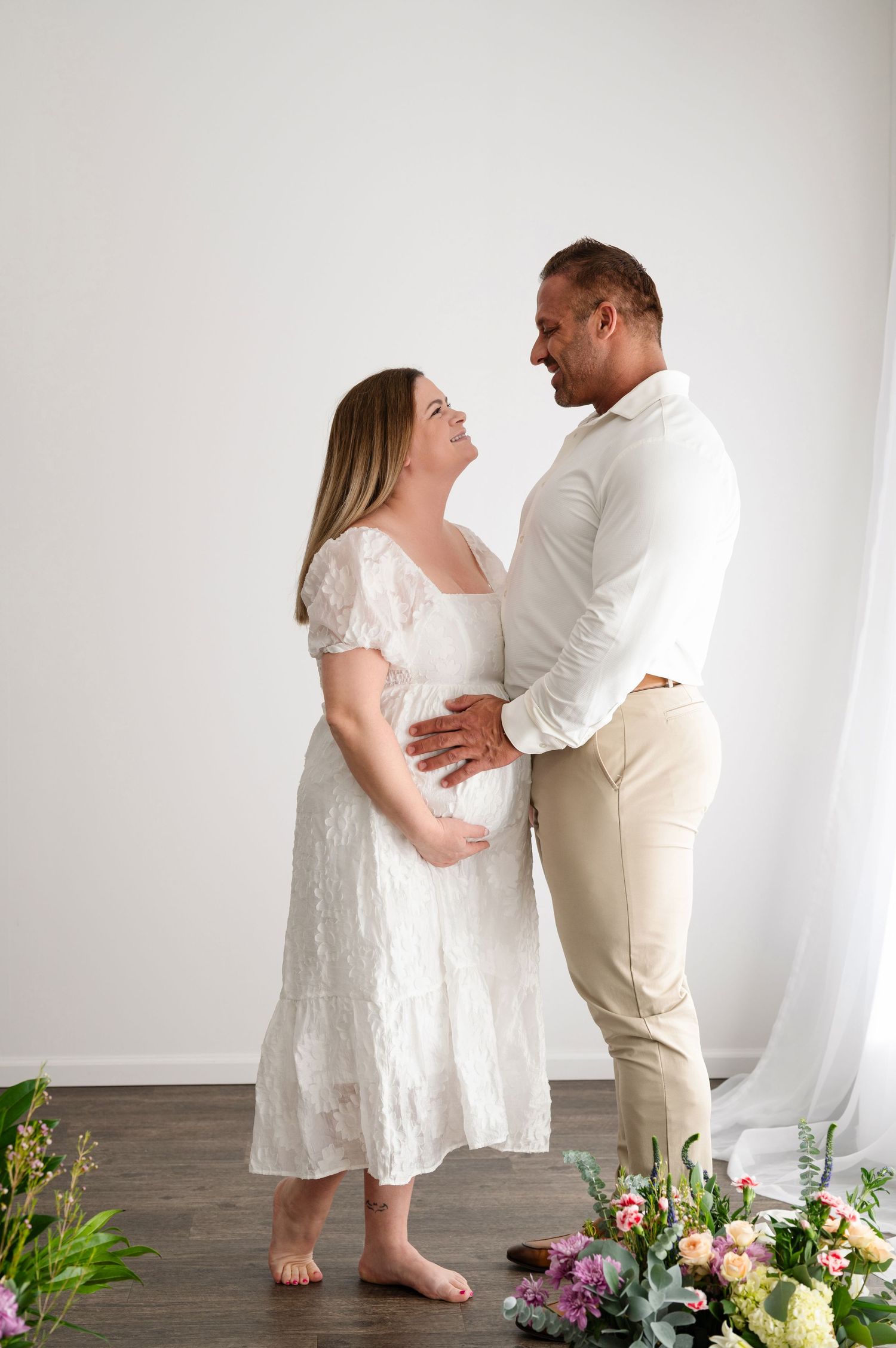 A couple shares an intimate moment during their maternity photoshoot with floral decorations.