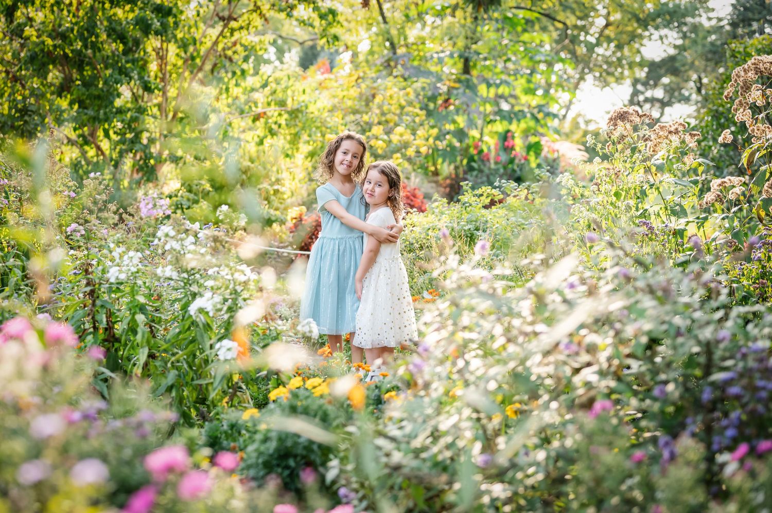 Sisters embrace in a lush garden with beautiful flowers surrounding them.