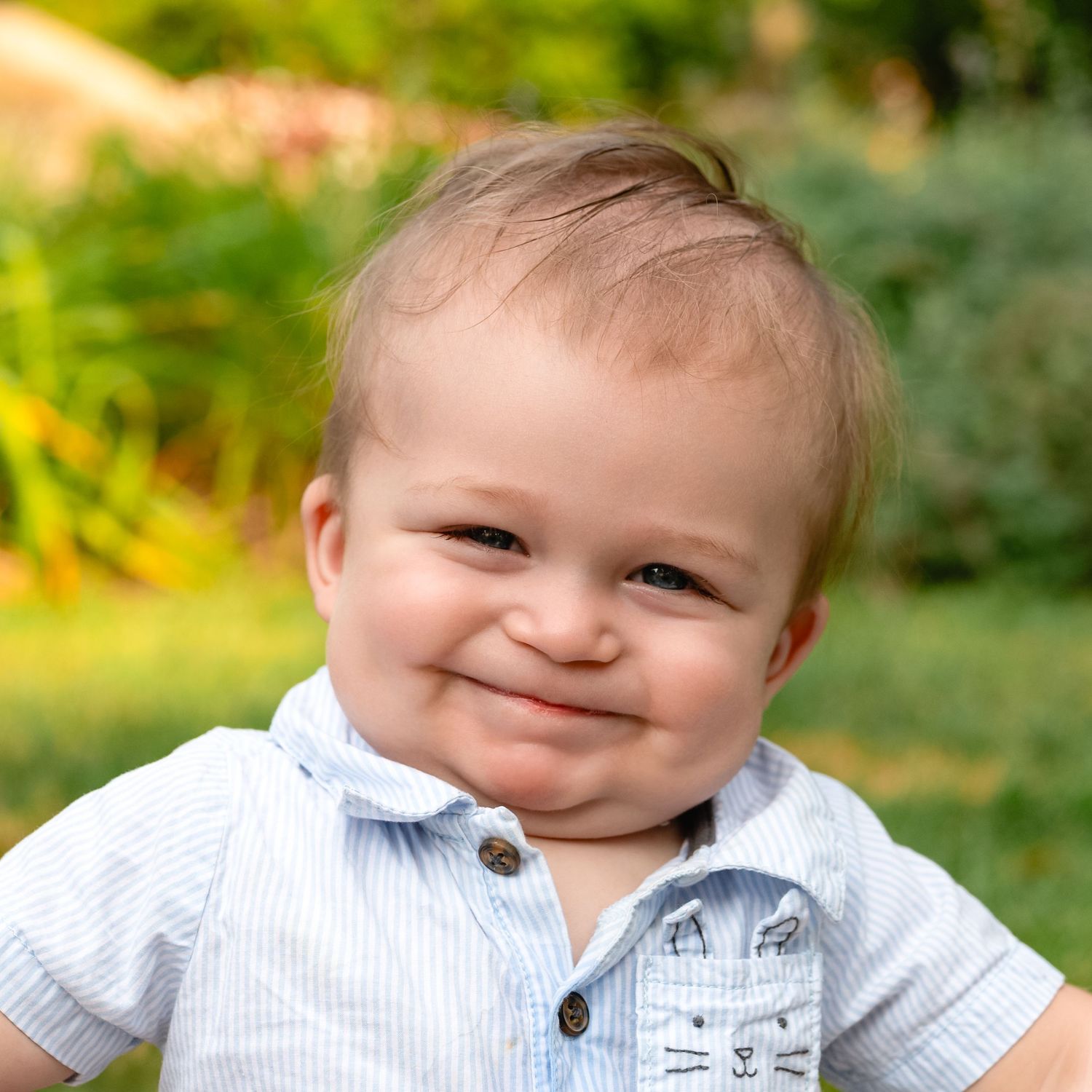 Baby wearing striped shirt showing sweet expression in outdoor portrait.