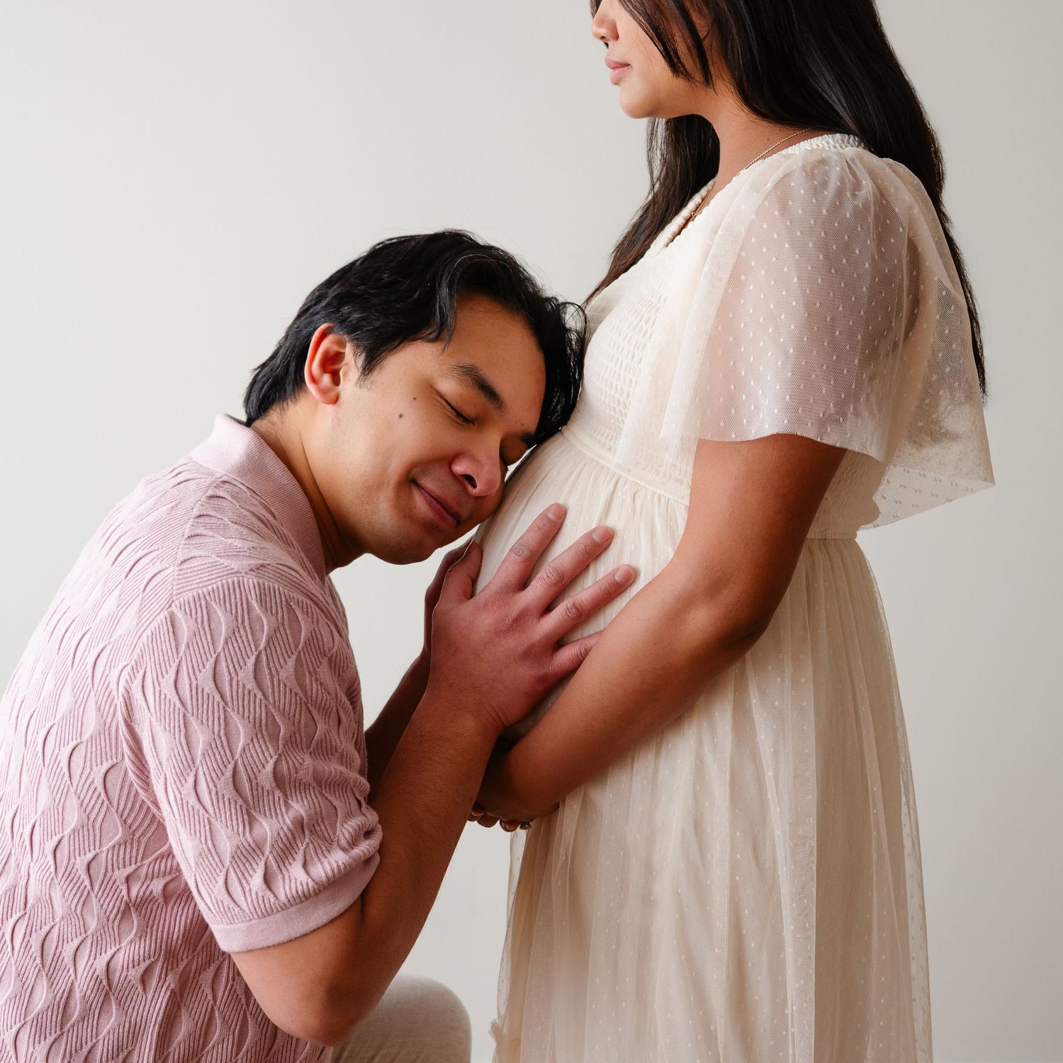 Intimate maternity photos showing tender moments against white backdrop.