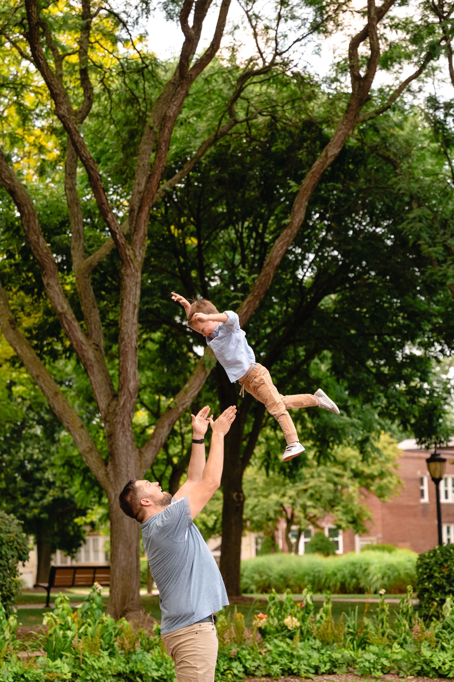 A playful moment captured in a lush garden as a child is tossed high into the air against a backdrop of green trees.