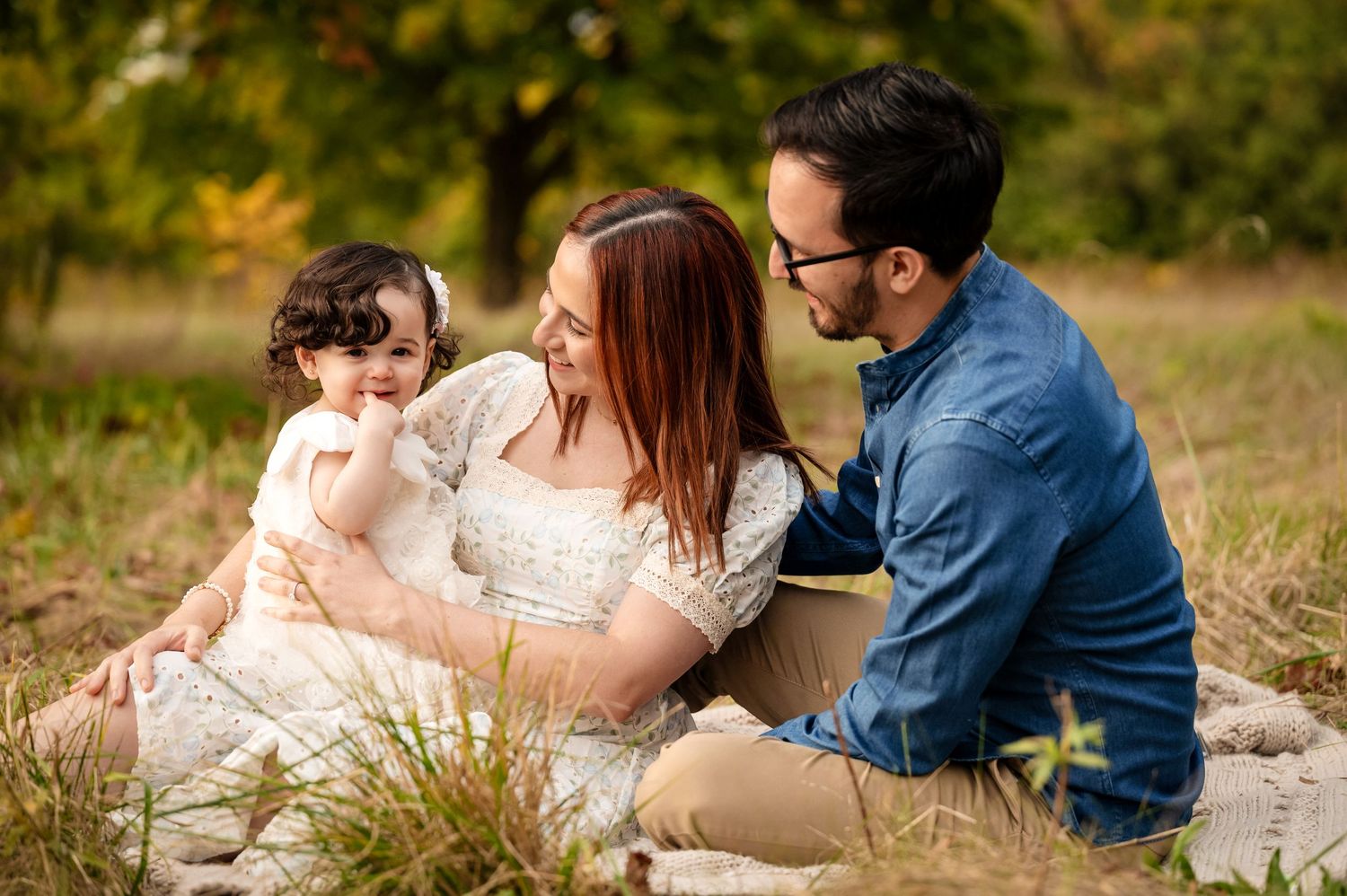 A family sits together on a blanket in a golden autumn field.
