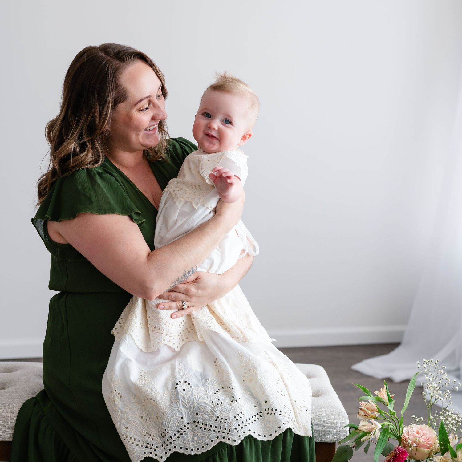 A tender moment captured between two figures in a green dress and white christening gown against a light background.