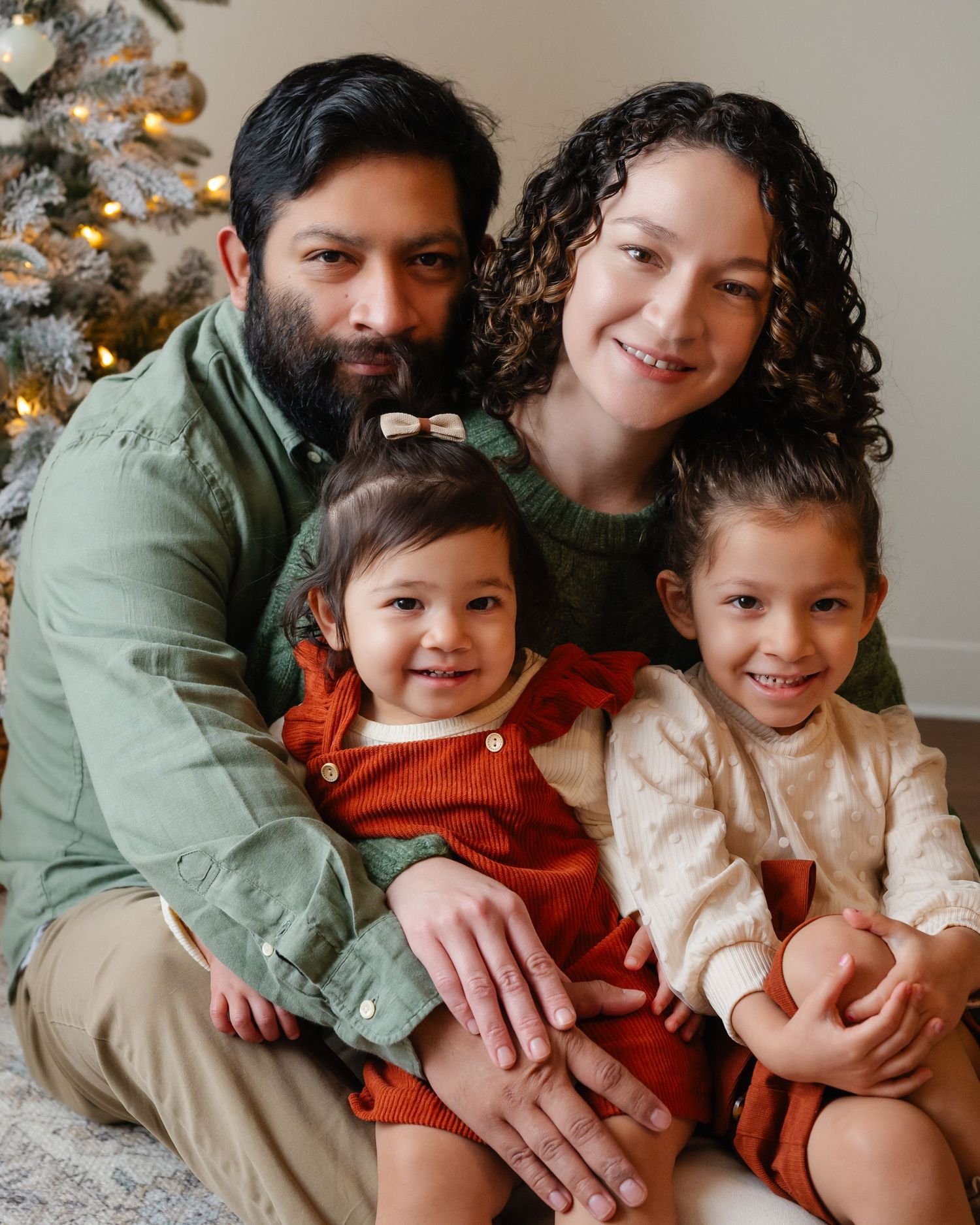 Family group shares warm embrace while sitting together by Christmas tree.