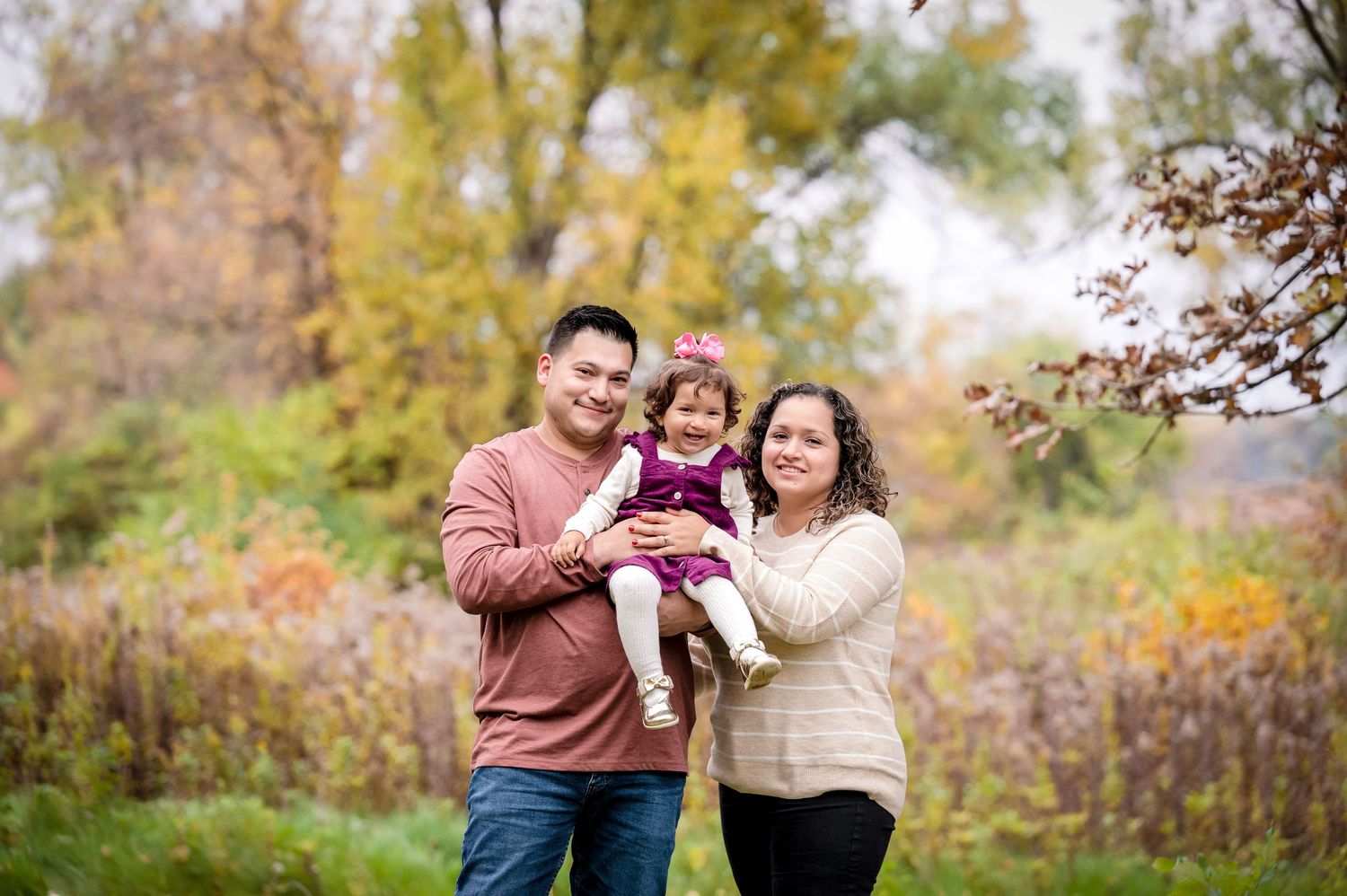 A couple holds their toddler during a fall session at a local forest preserve.