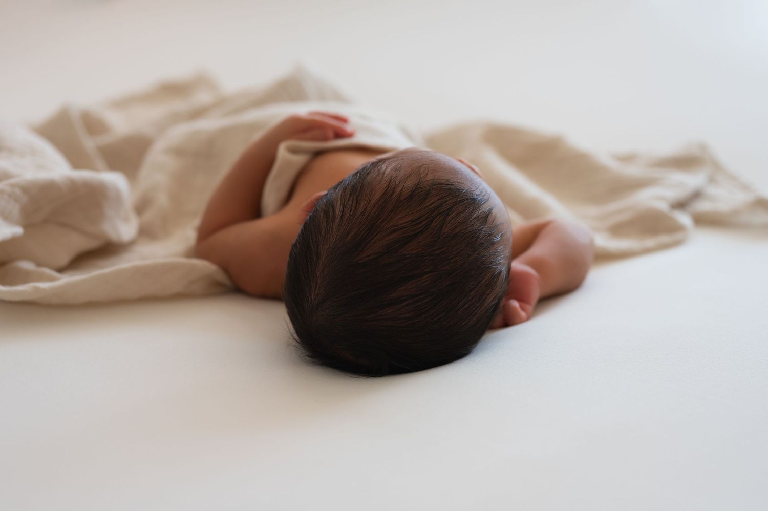 Peaceful sleeping newborn on cream colored blanket against white background.