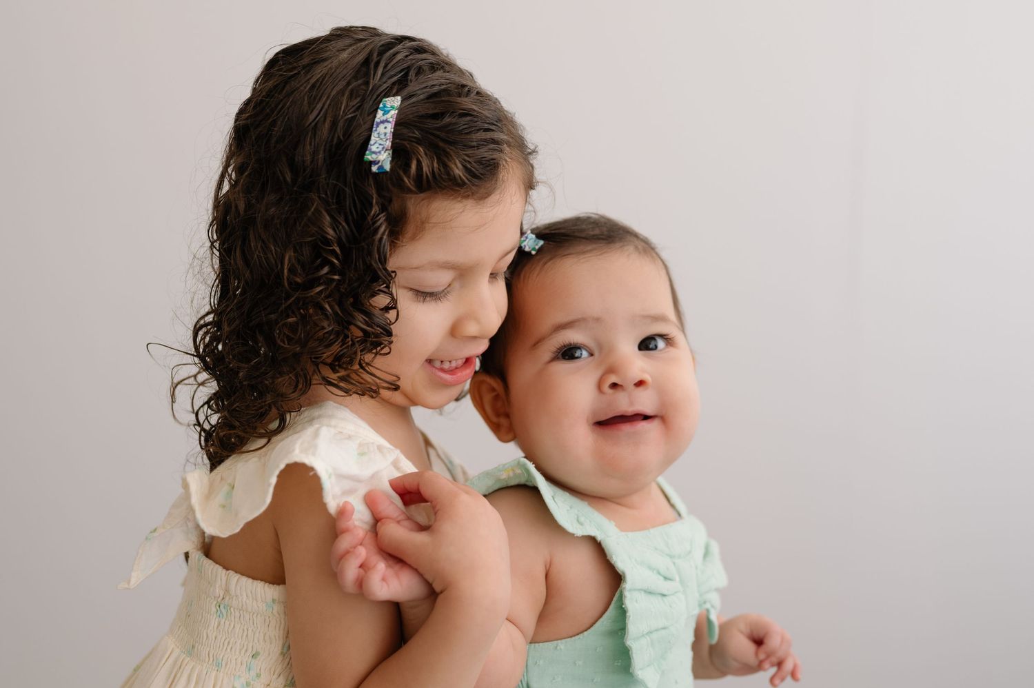 Sweet sibling interaction captured in soft lighting against white background.